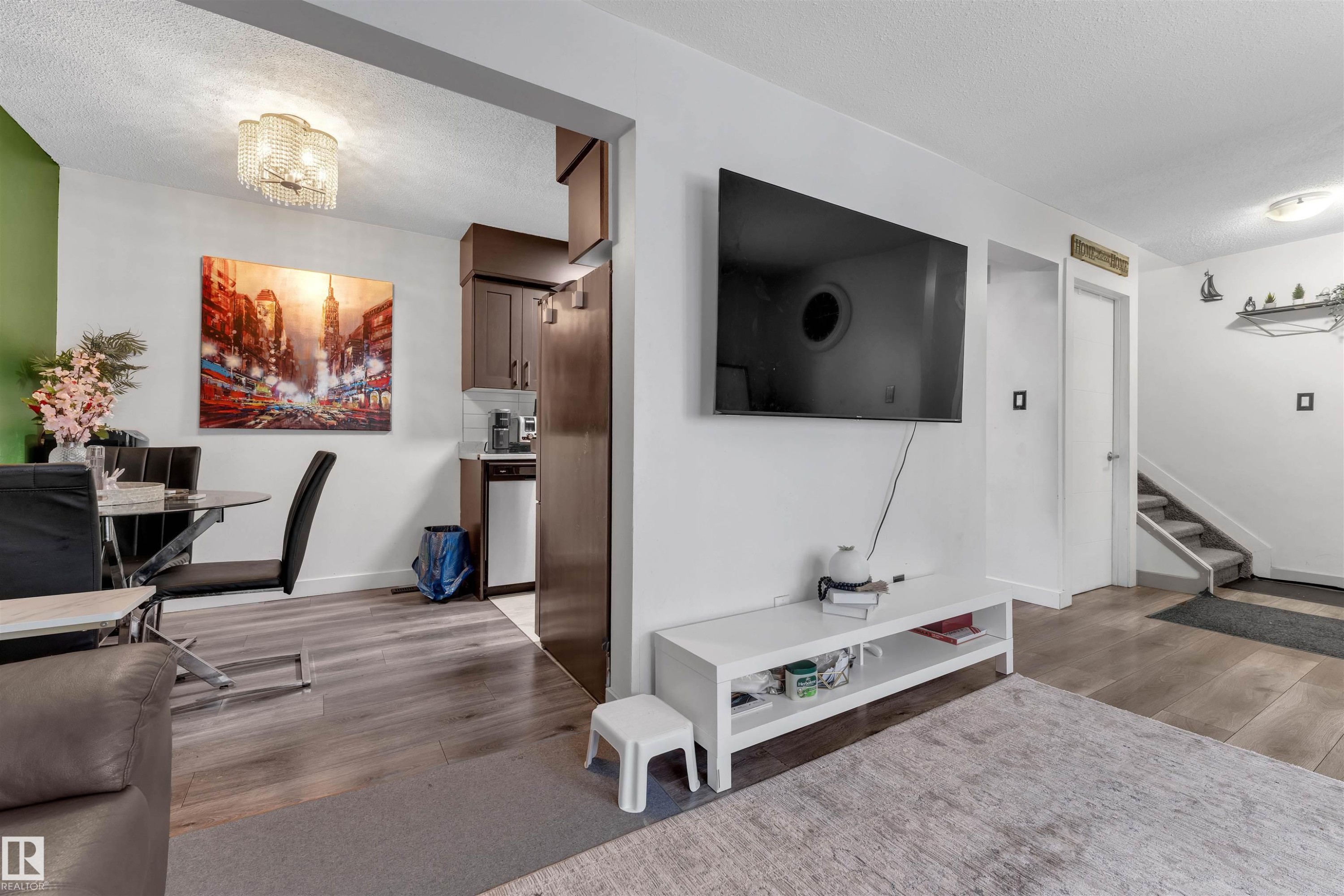 Open-concept living area featuring wood-finish flooring, a contemporary ceiling light fixture, a dedicated dining space with a glass-top table, and a kitchen area with dark wood cabinetry - 7 14115 82 Street, Edmonton, AB - Indoor