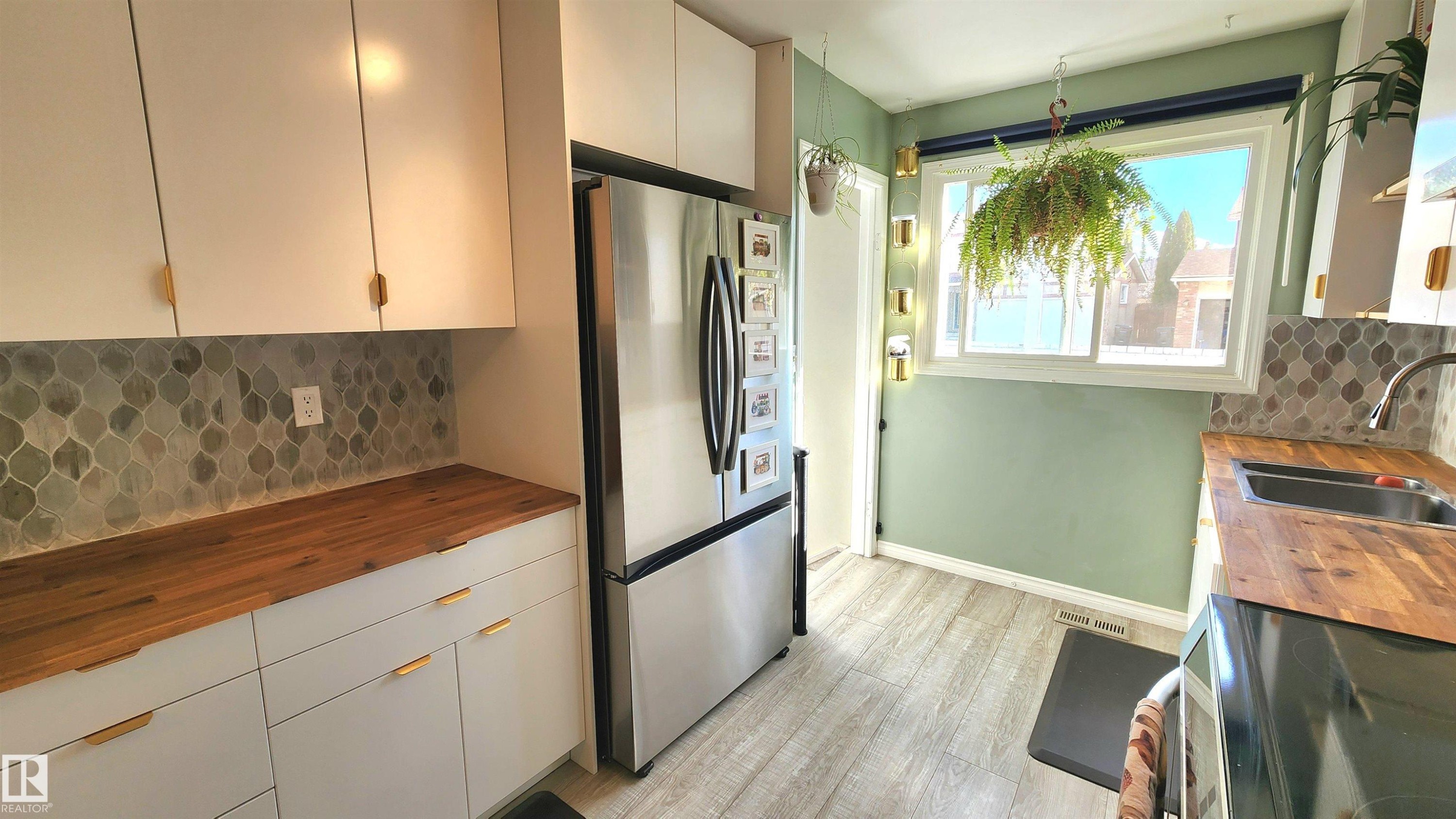 Kitchen featuring wood-finish countertops, white cabinetry with brass hardware, and a patterned tile backsplash - 3531 46 Street, Edmonton, AB - Indoor Photo Showing Kitchen With Double Sink