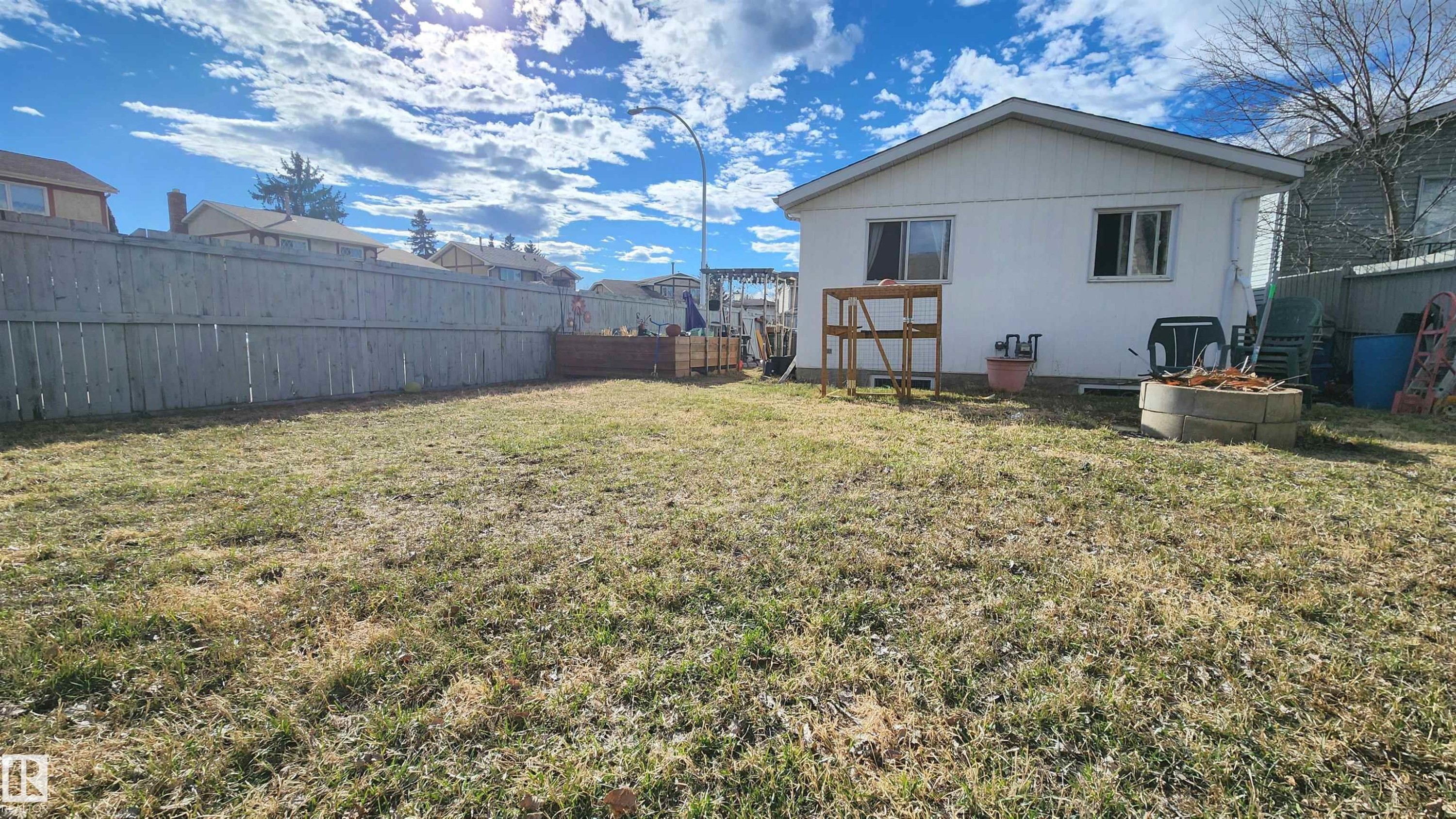 Expansive backyard featuring a large grass area, a full-height perimeter fence, and a white exterior building with multiple windows - 3531 46 Street, Edmonton, AB - Outdoor