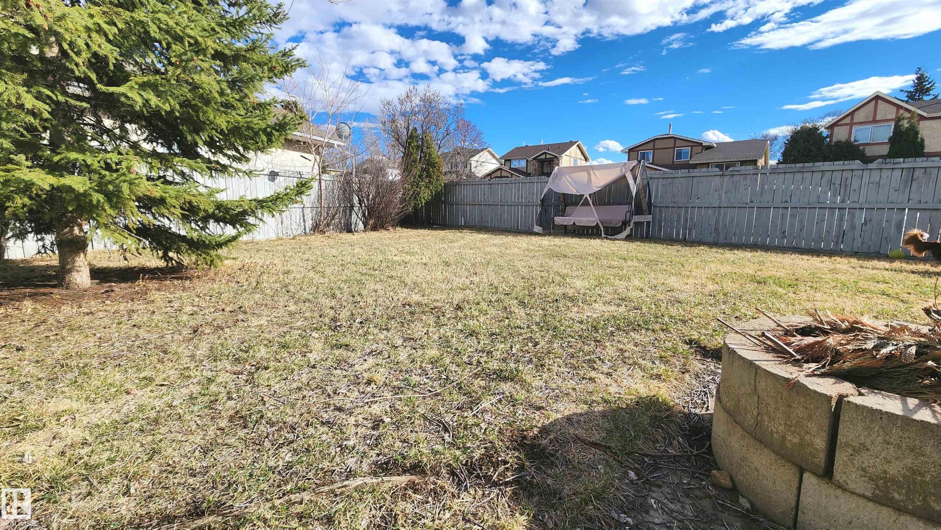 Spacious backyard featuring a full perimeter privacy fence, mature evergreen tree, and a built-in stone fire pit - 3531 46 Street, Edmonton, AB - Outdoor