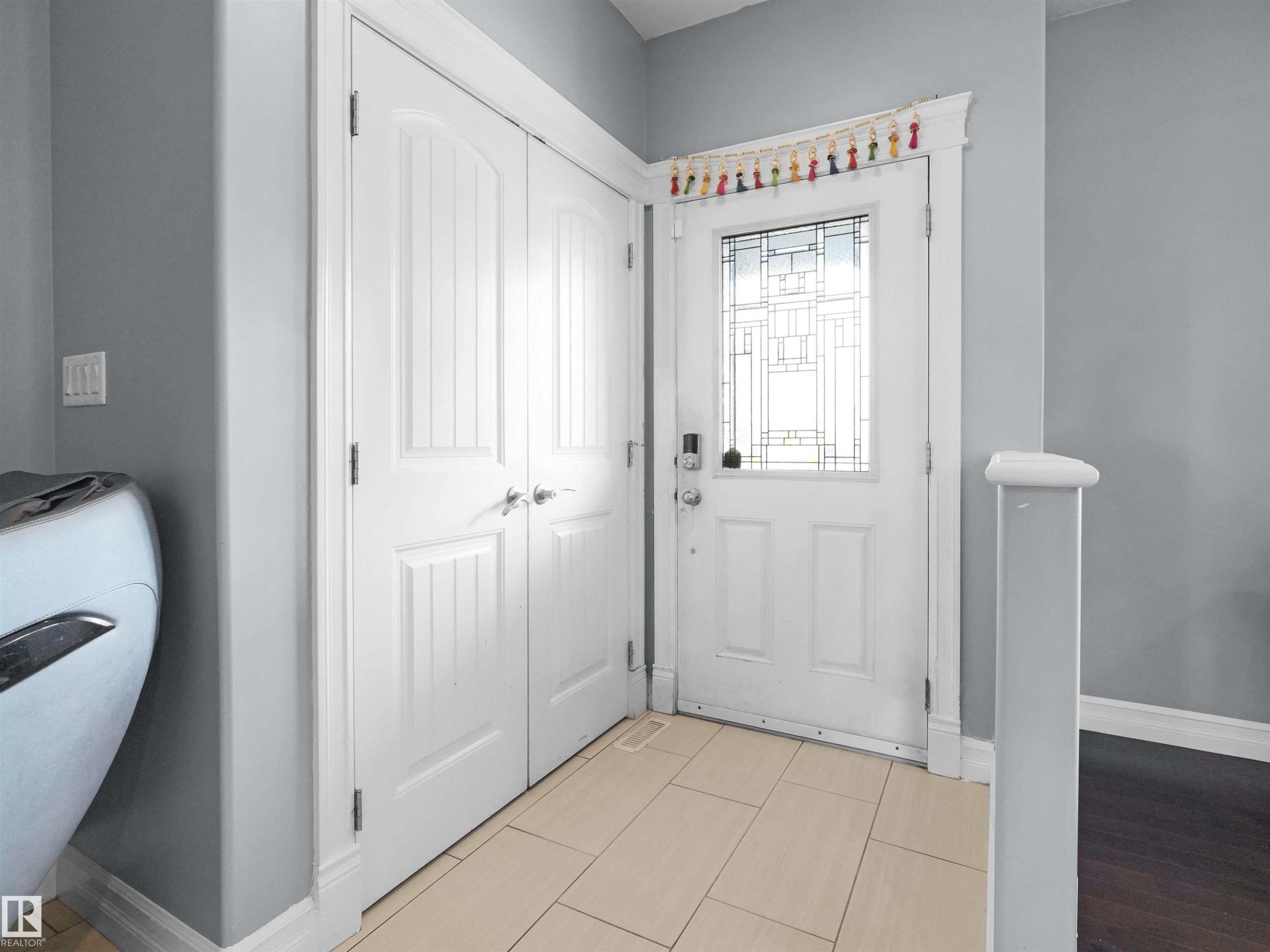 Entryway featuring a white paneled door with decorative glass inserts, light tile flooring, and a double bi-fold closet with brushed nickel hardware - 5192 1B Avenue Sw, Edmonton, AB - Indoor Photo Showing Other Room