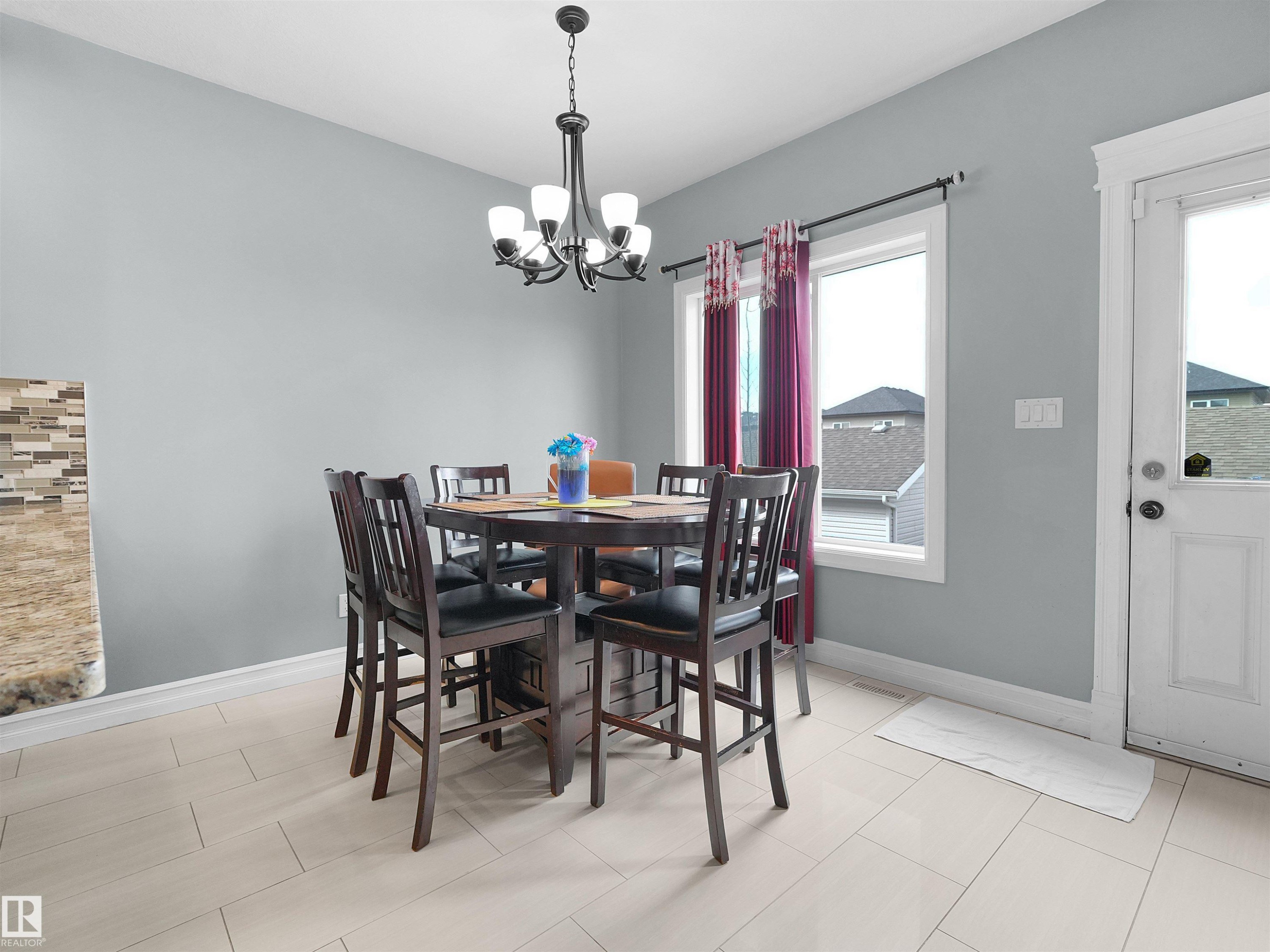 Dining area featuring light-toned tile flooring, a multi-light chandelier, a window with white trim, and a white paneled door - 5192 1B Avenue Sw, Edmonton, AB - Indoor Photo Showing Dining Room
