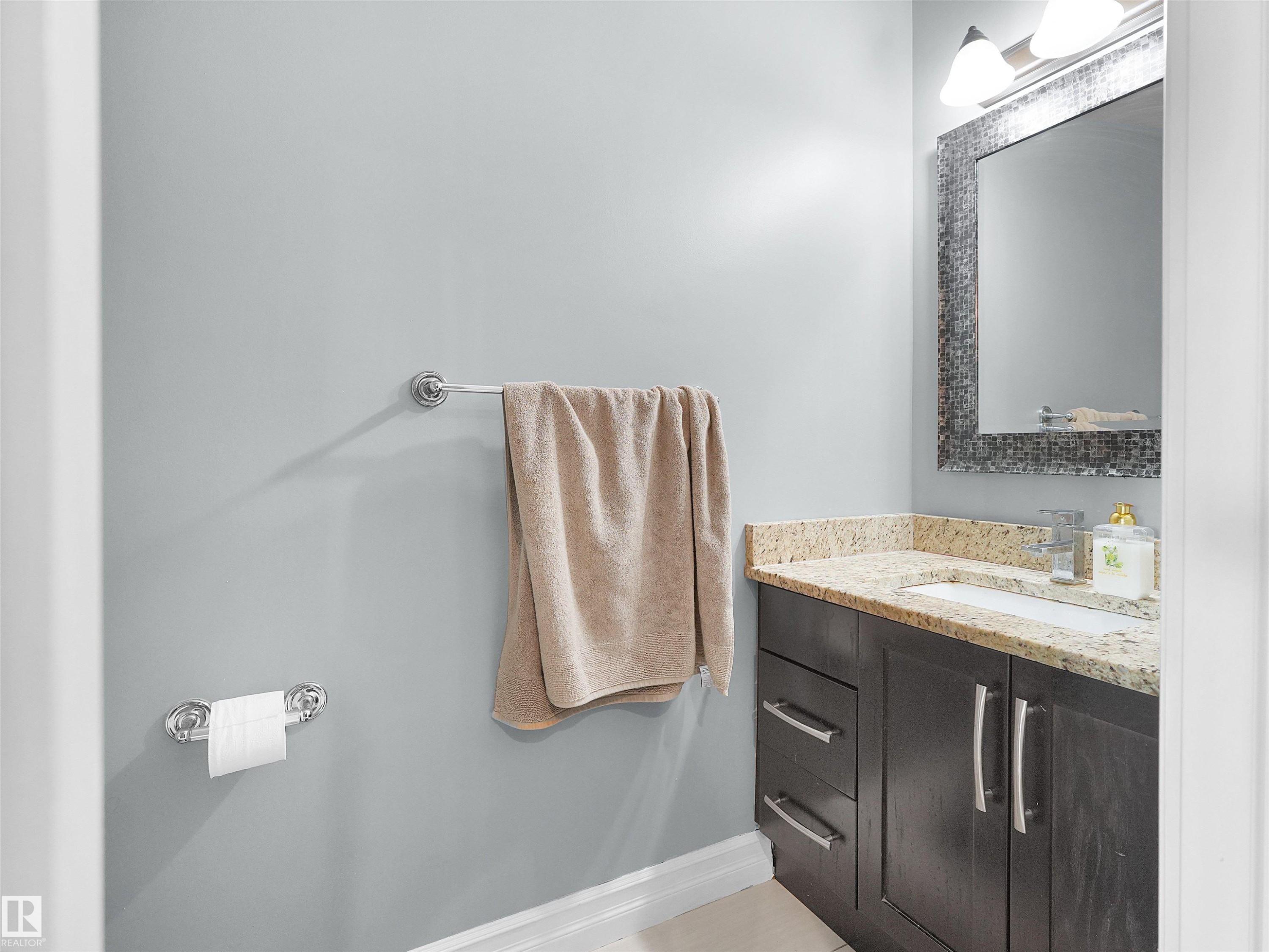 Bathroom vanity featuring a light-colored countertop, undermount sink, dark wood-finish cabinetry, and brushed nickel hardware - 5192 1B Avenue Sw, Edmonton, AB - Indoor Photo Showing Bathroom