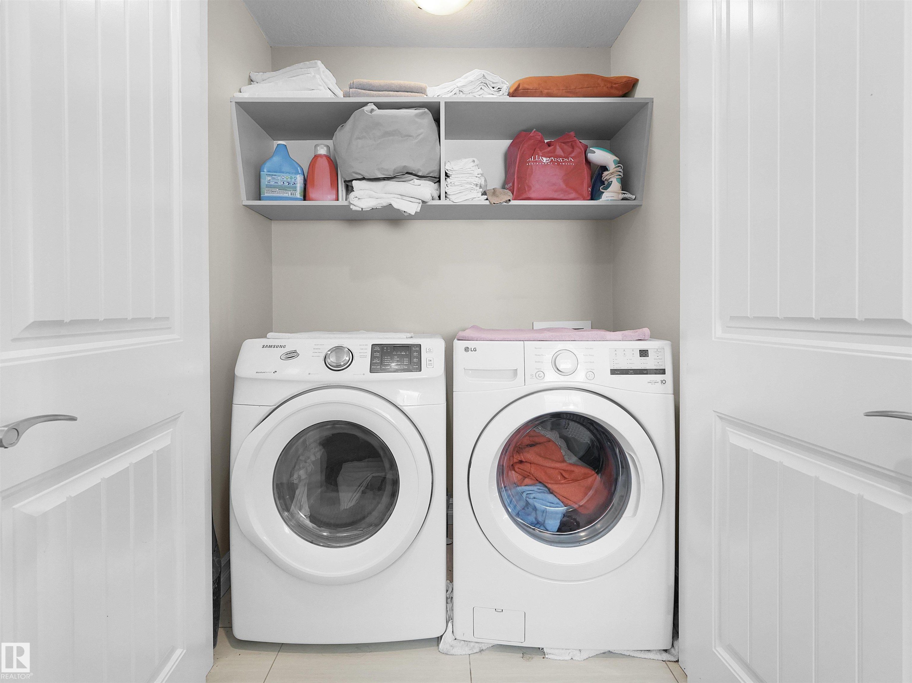 Dedicated laundry area featuring a front-loading washer and dryer, overhead shelving, and neutral wall paint - 5192 1B Avenue Sw, Edmonton, AB - Indoor Photo Showing Laundry Room