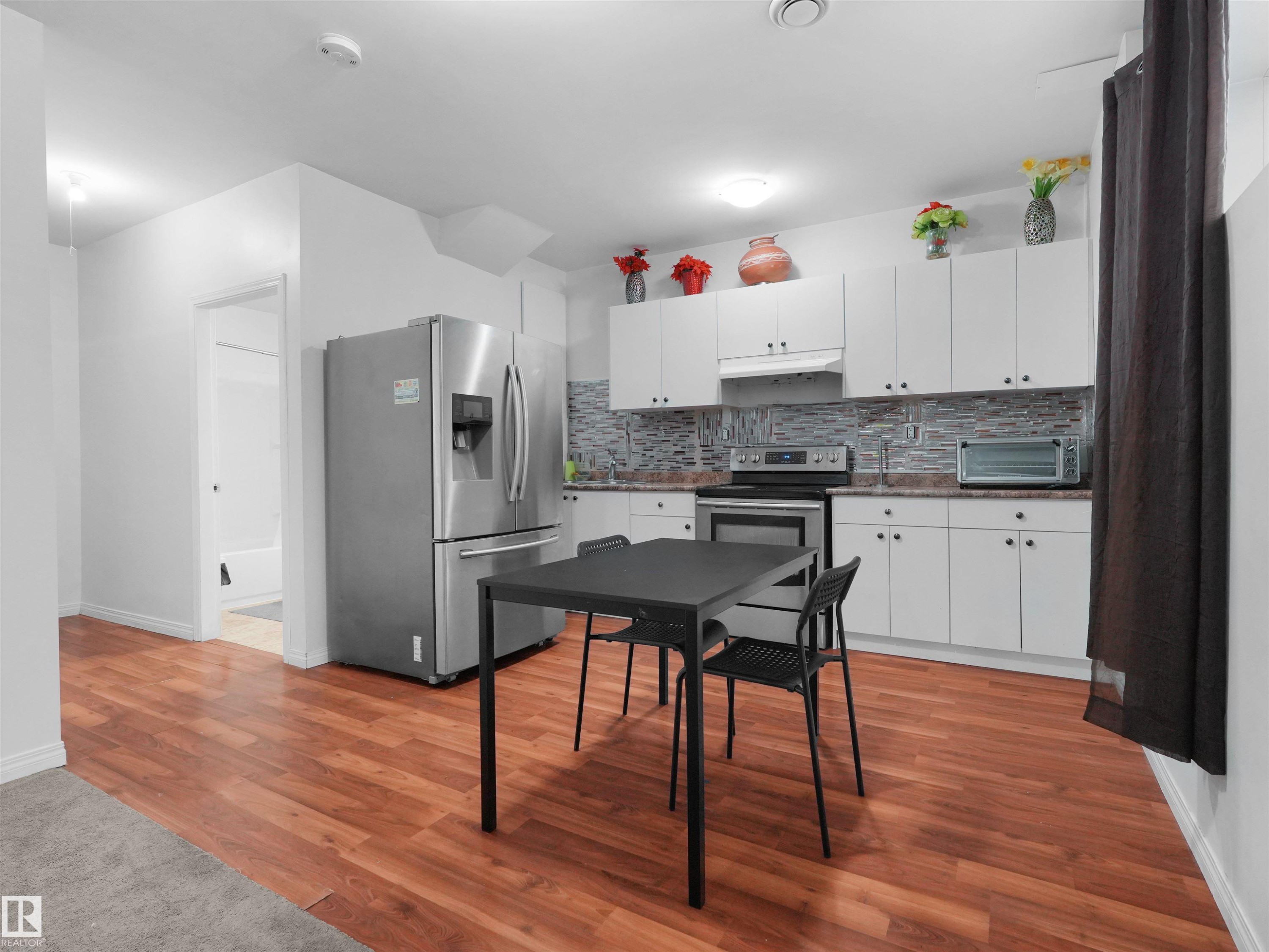 Kitchen featuring white cabinetry, stone-look countertops, a tile backsplash, and stainless steel appliances - 5192 1B Avenue Sw, Edmonton, AB - Indoor Photo Showing Kitchen