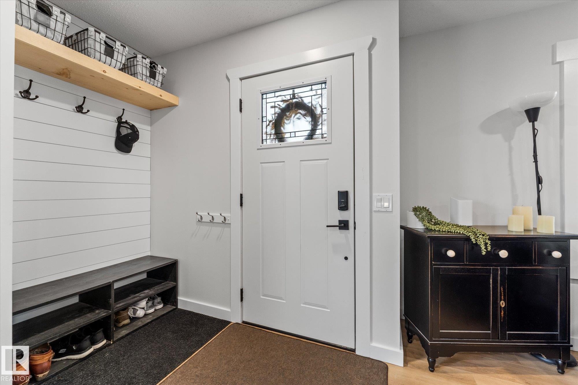 The inviting entryway features a white paneled wall with a natural wood shelf, a dark wood bench with shoe storage, and a white entry door with decorative glass - 3908 44 Avenue, Stony Plain, AB - Indoor Photo Showing Other Room