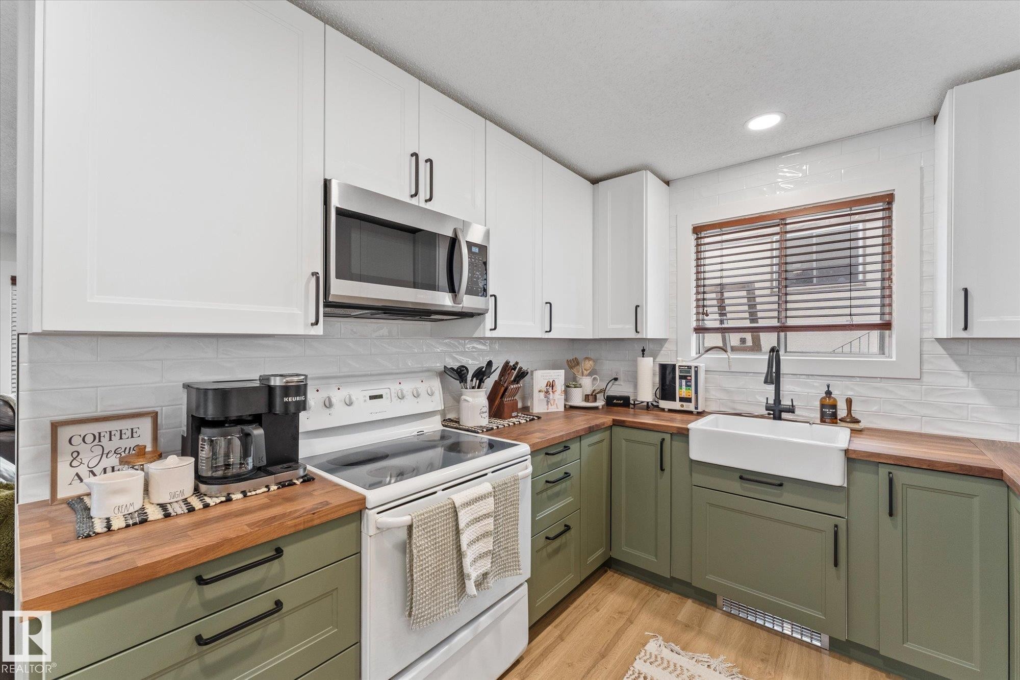 The kitchen features two-toned cabinetry, with white upper cabinets and green lower cabinets, complemented by wooden countertops - 3908 44 Avenue, Stony Plain, AB - Indoor Photo Showing Kitchen