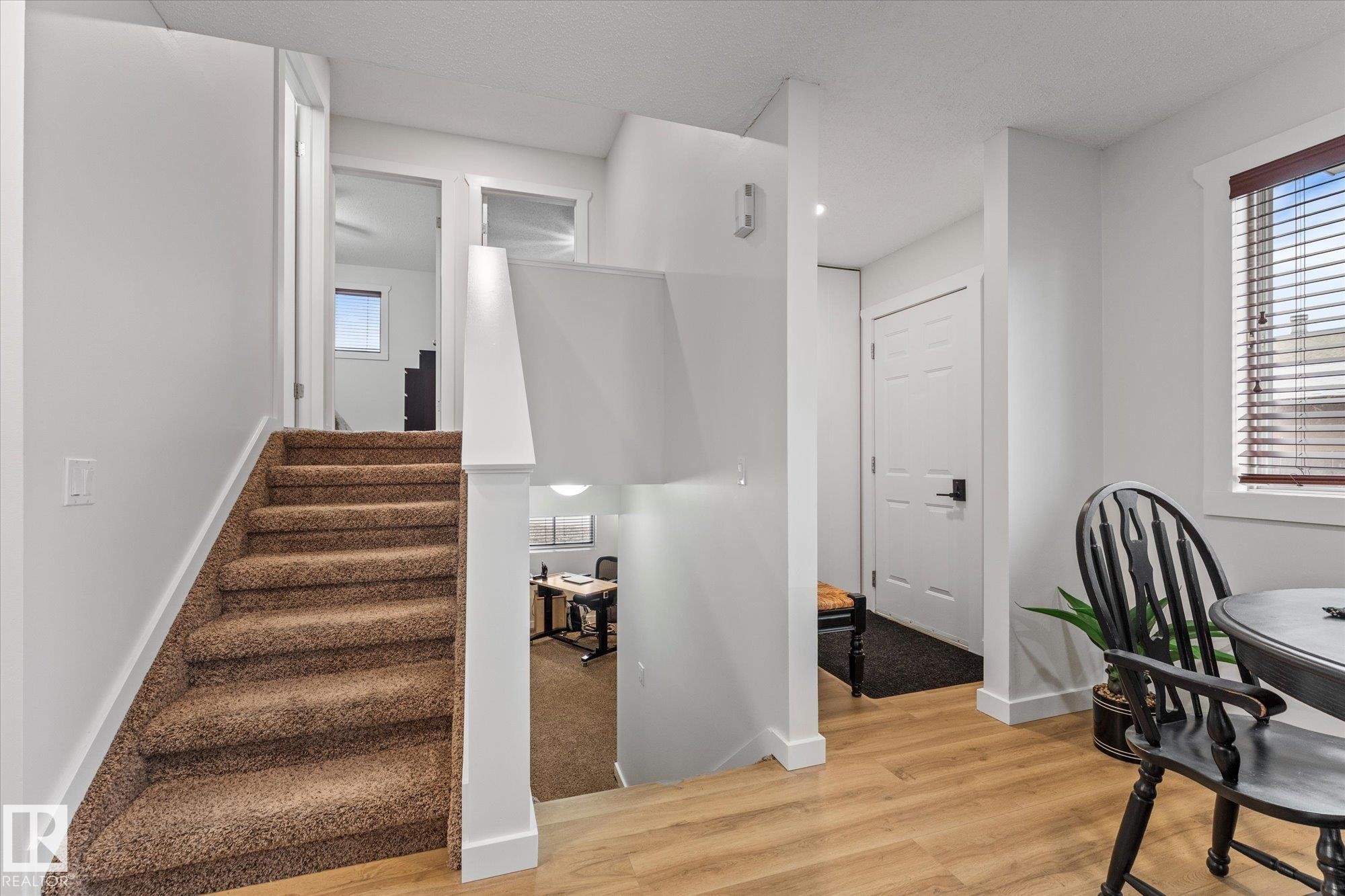 Interior hallway featuring light wood flooring, a carpeted staircase, and a doorway leading to a separate room - 3908 44 Avenue, Stony Plain, AB - Indoor Photo Showing Other Room