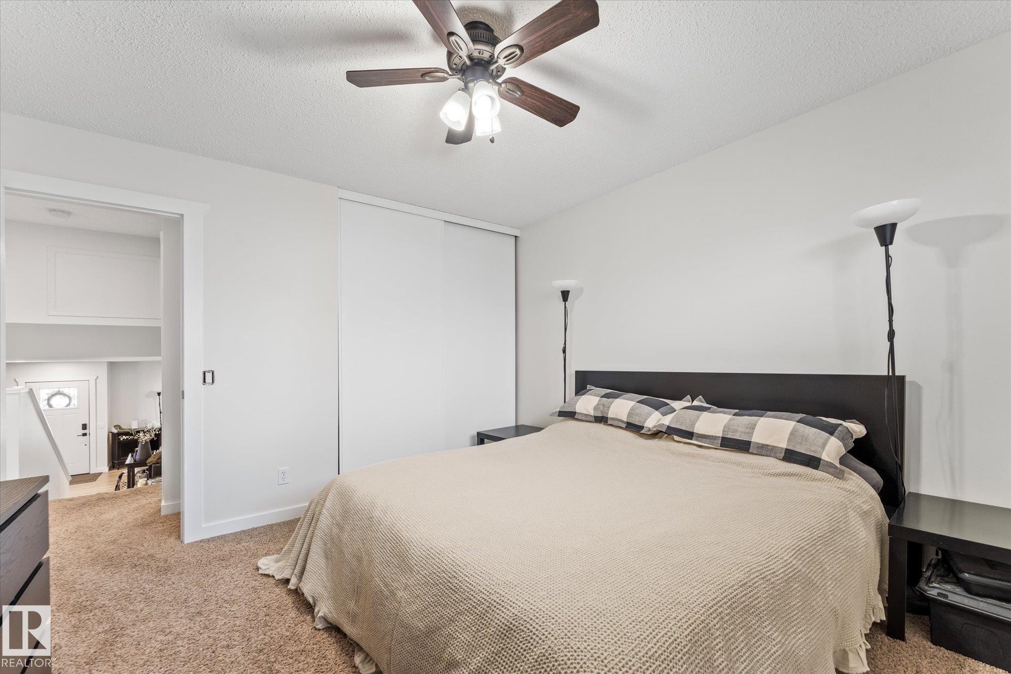 The property features a bedroom with a ceiling fan, carpeted flooring, and a large sliding door closet - 3908 44 Avenue, Stony Plain, AB - Indoor Photo Showing Bedroom