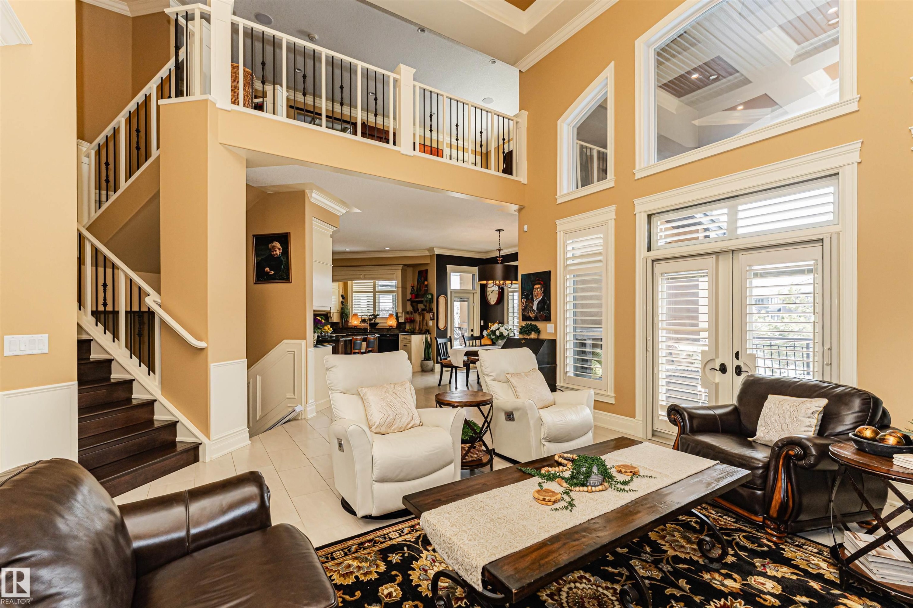 Grand living area featuring high ceilings, large windows with shutters, and a prominent staircase with a balcony overlooking the space - 3048 Watson Landing, Edmonton, AB - Indoor Photo Showing Living Room