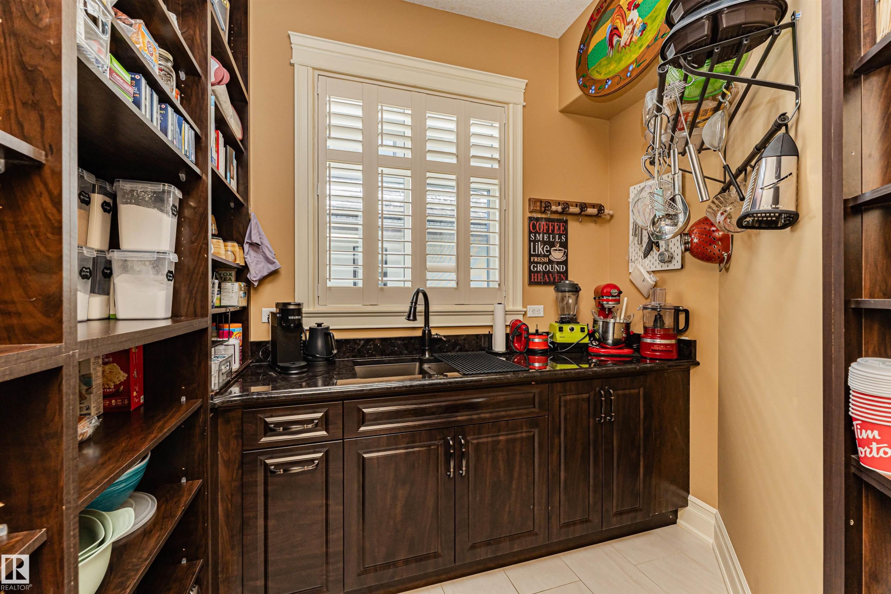 This well-appointed pantry features extensive dark wood shelving, a built-in counter with a sink, and dark granite countertops. formally known as a butler pantry. - 3048 Watson Landing, Edmonton, AB - Indoor Photo Showing Other Room