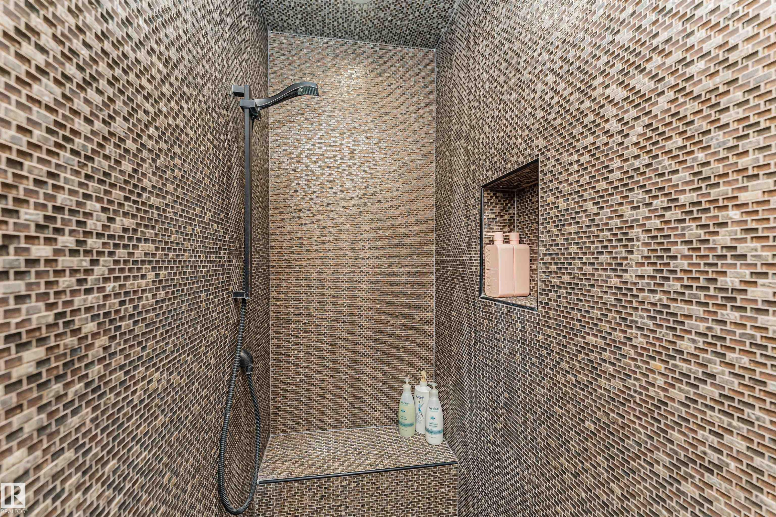 The shower features a dark-toned shower fixture, mosaic wall tiling, and a built-in shower bench - 3048 Watson Landing, Edmonton, AB -