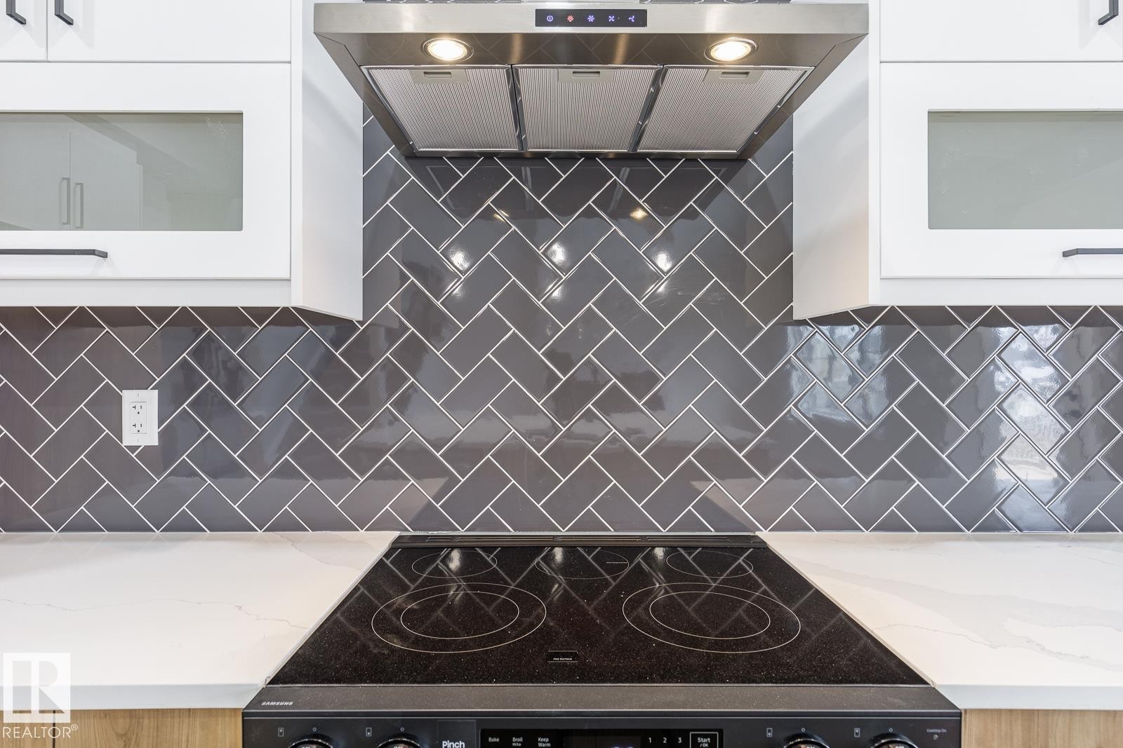 Modern kitchen featuring a herringbone pattern subway tile backsplash, white upper cabinetry with frosted glass inserts, and a stainless steel range hood - 917 Elderberry Landing, Edmonton, AB - Indoor