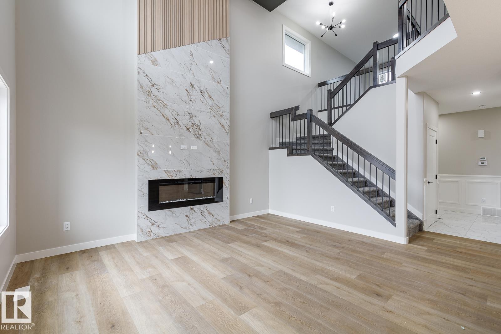 Living area featuring a floor-to-ceiling fireplace with a marble-look surround and integrated linear electric fireplace, complemented by vertical wood-finish paneling - 917 Elderberry Landing, Edmonton, AB - Indoor With Fireplace