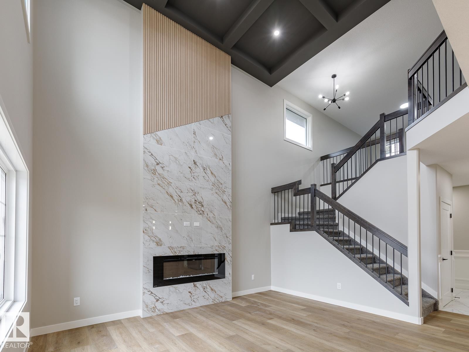 Two-story living area featuring a full-height fireplace with an electric insert, light-toned wood-finish flooring, and a coffered ceiling - 917 Elderberry Landing, Edmonton, AB - Indoor With Fireplace