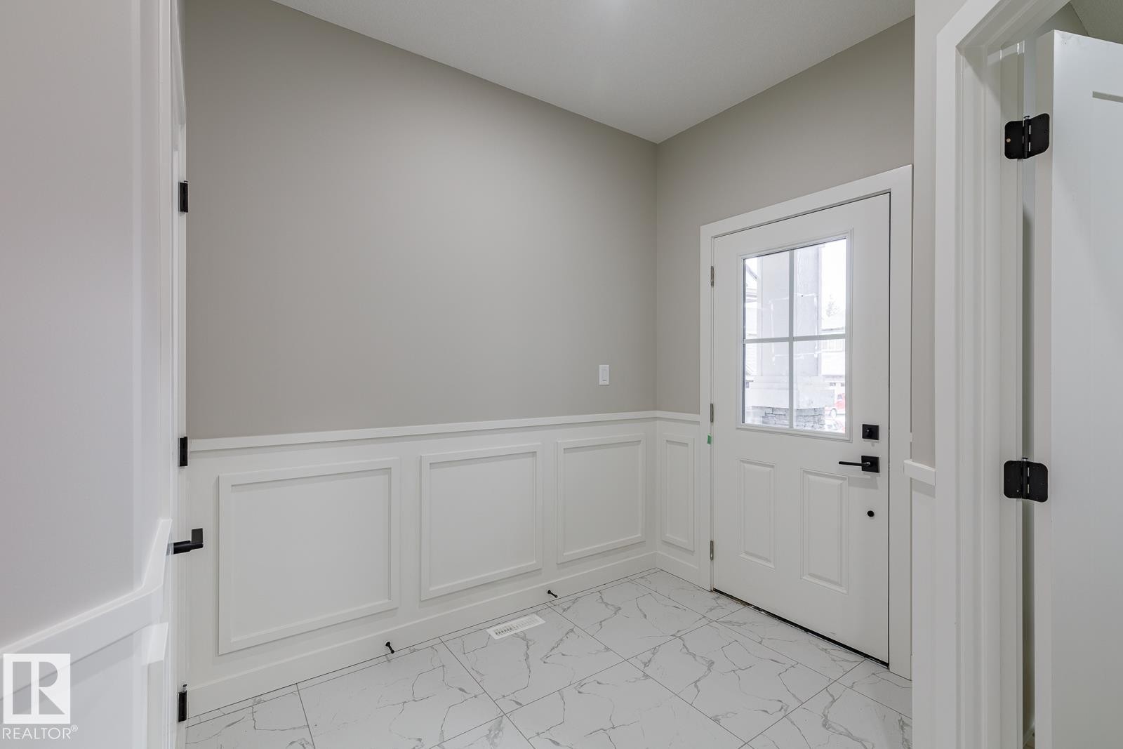 Entryway featuring panel molding wainscoting, a white paneled door with a multi-pane window, and large format marble-look tile flooring - 917 Elderberry Landing, Edmonton, AB - Indoor Photo Showing Other Room