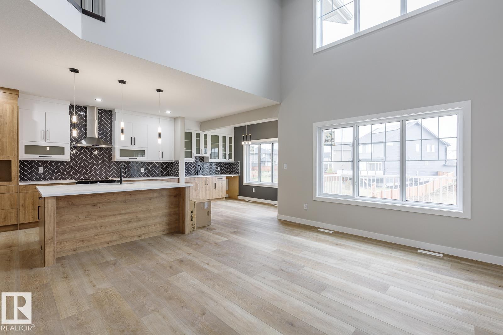 Expansive open-concept living area featuring a kitchen island with a light wood-finish base and light-toned countertop, contrasting dark herringbone backsplash, and pendant lighting - 917 Elderberry Landing, Edmonton, AB - Indoor