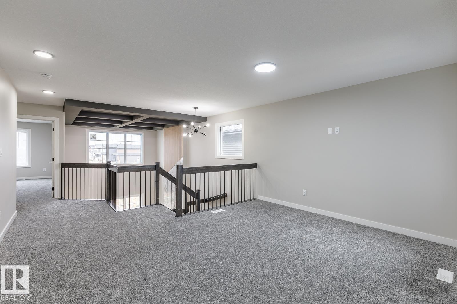 Spacious second-story landing featuring gray carpet, a dark wood-finish railing with vertical spindles, and a dark wood-finish coffered ceiling accent - 917 Elderberry Landing, Edmonton, AB - Indoor Photo Showing Other Room