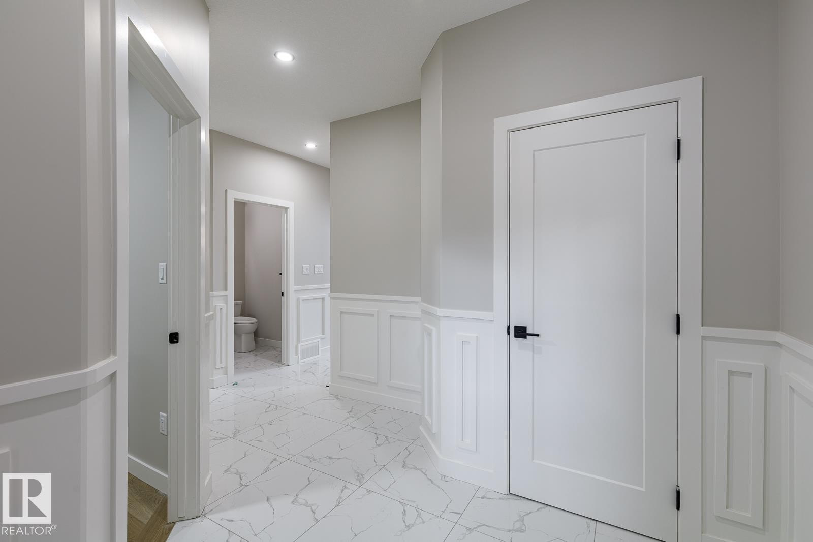 Hallway featuring marble-look tile flooring, white wainscoting, flush-panel doors with black hardware, and recessed lighting - 917 Elderberry Landing, Edmonton, AB - Indoor Photo Showing Other Room