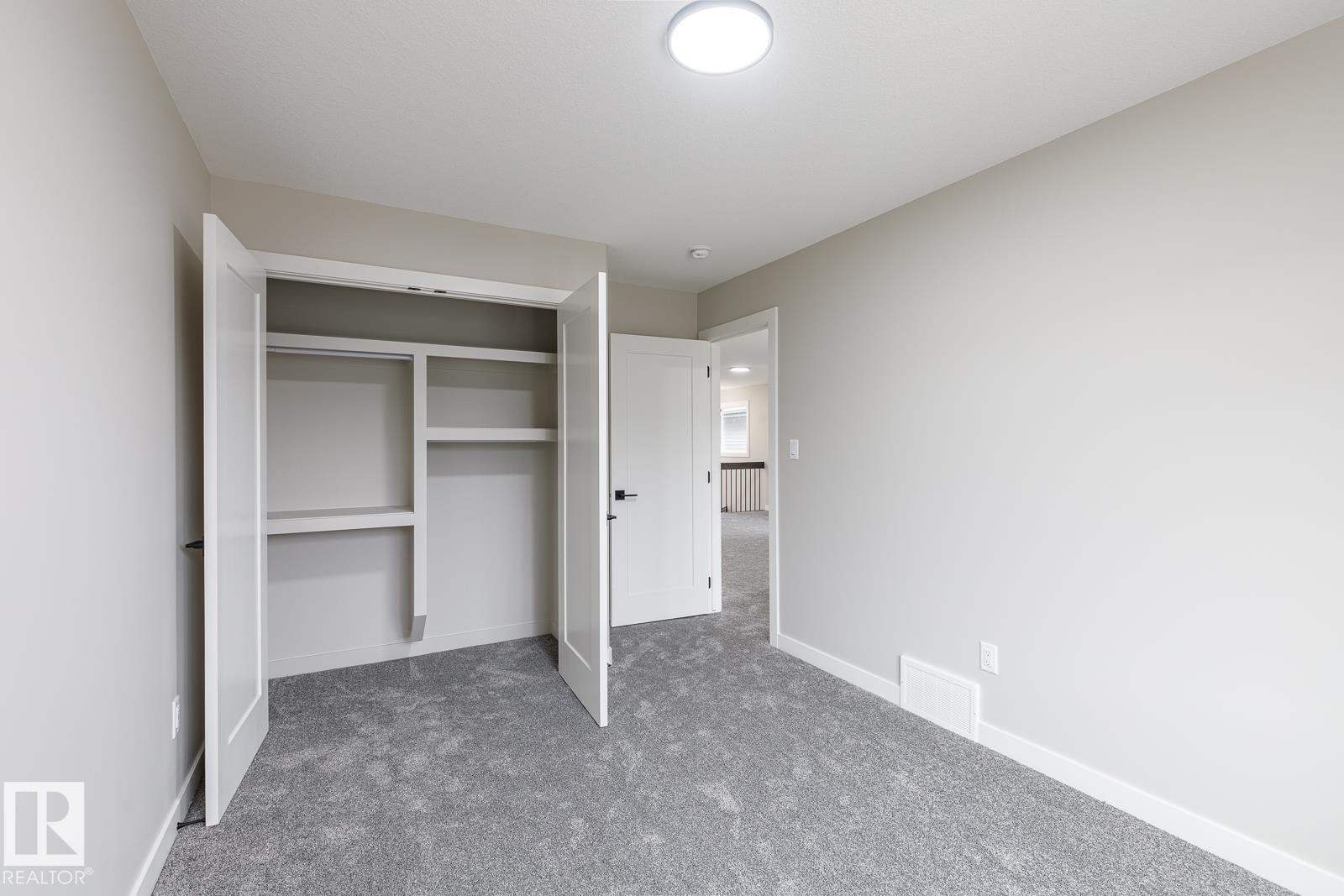 Interior room featuring neutral wall paint, gray carpeting, a built-in closet with double doors and shelving, and a flush-mount ceiling light fixture - 917 Elderberry Landing, Edmonton, AB - Indoor Photo Showing Other Room