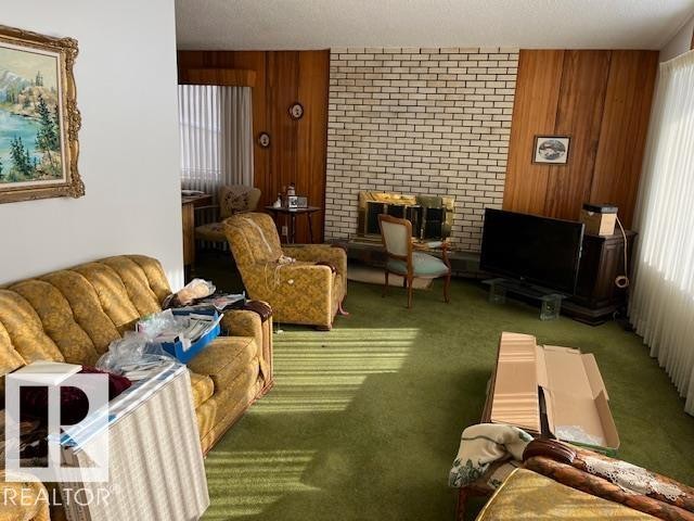 Living room featuring a fireplace with a brick surround, wood paneling, and a large window providing natural light - 11003 144 Street, Edmonton, AB - Indoor Photo Showing Other Room