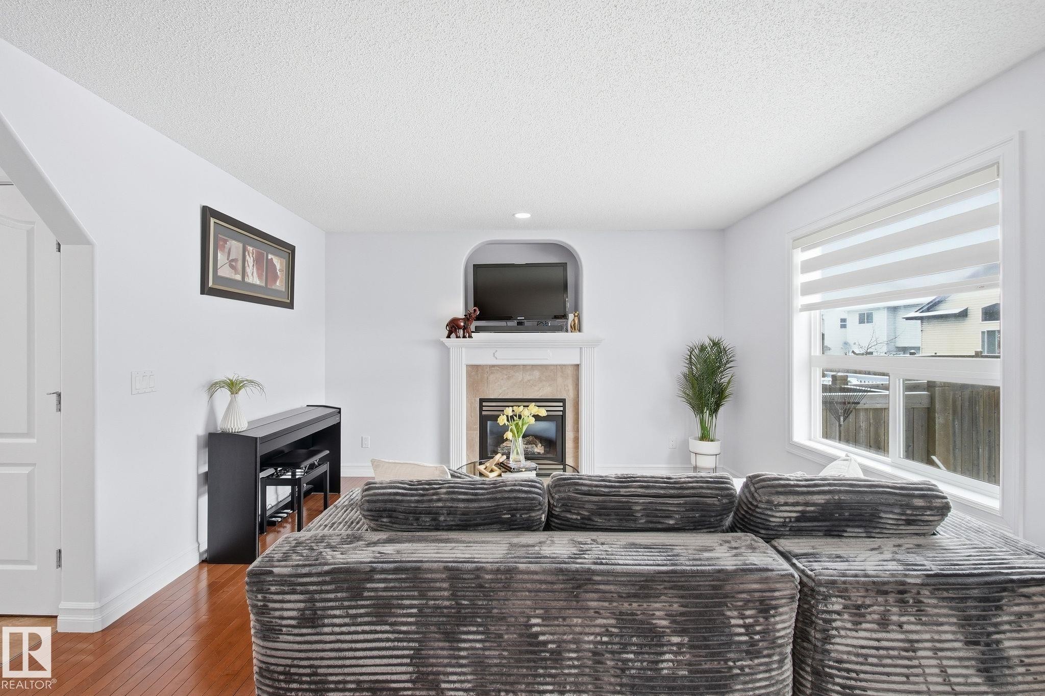 Living area featuring a fireplace with a stone surround and white mantel, a built-in arched alcove, and wood-finish flooring - 3016 24 Ave, Edmonton, AB - Indoor With Fireplace