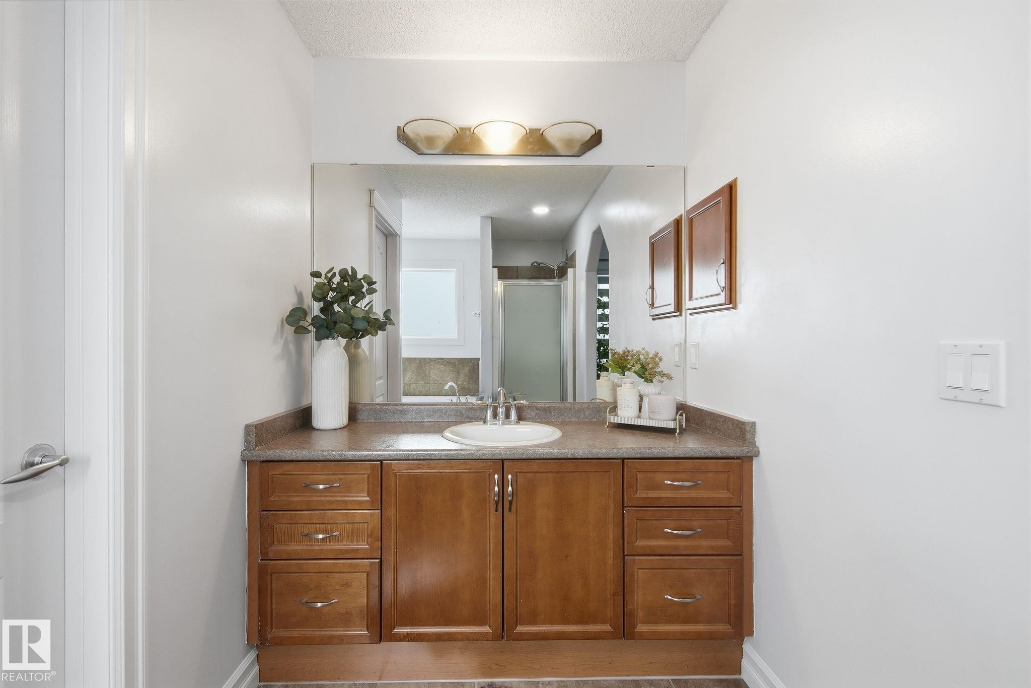 Bathroom vanity featuring a light brown countertop, an undermount sink, and wood-finish cabinetry with multiple drawers - 3016 24 Ave, Edmonton, AB - Indoor