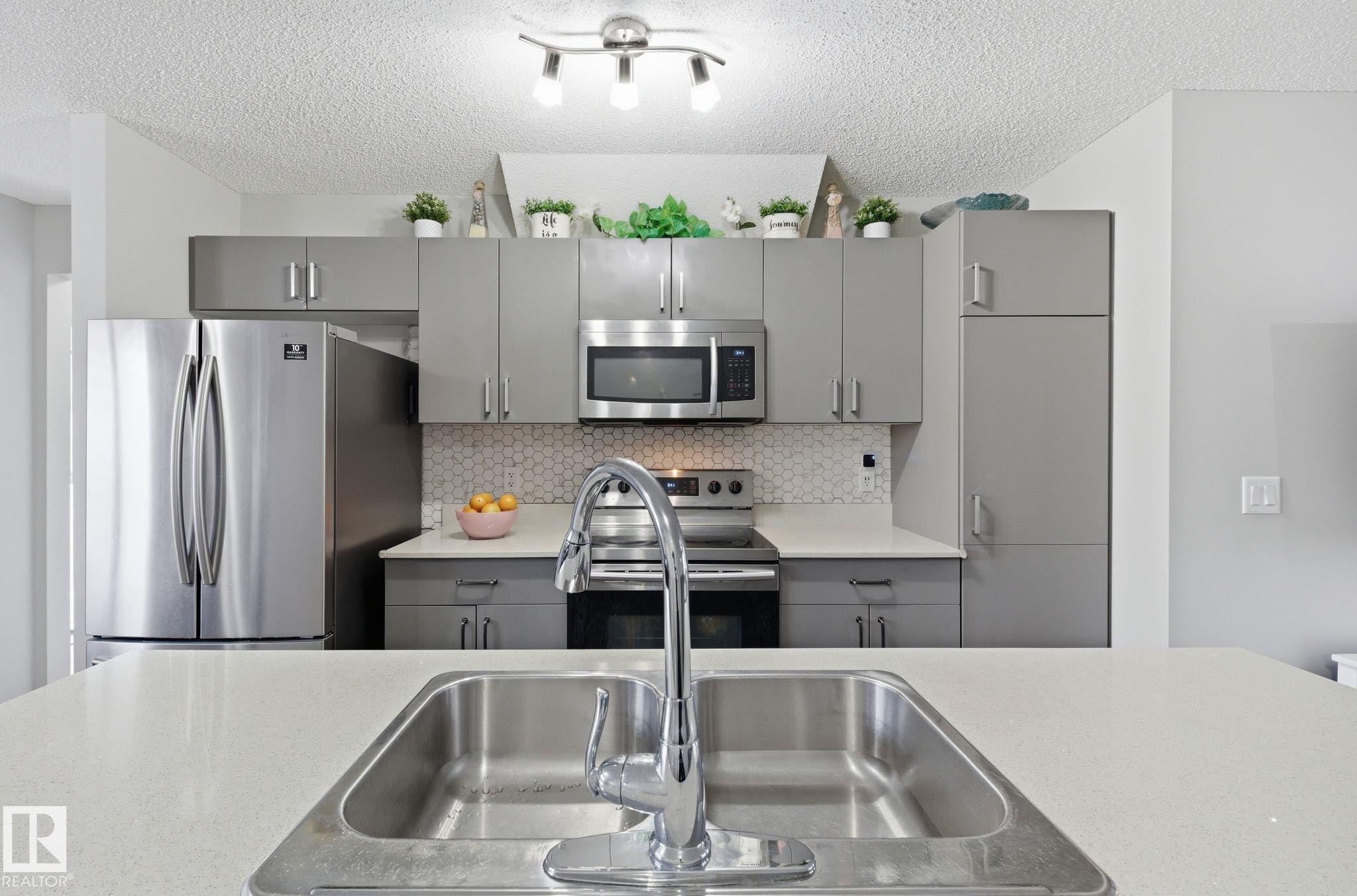 The kitchen features modern gray cabinetry, stainless steel appliances, a white hexagonal tile backsplash, and a large sink with a chrome faucet - 4636 175 Ave, Edmonton, AB - Indoor Photo Showing Kitchen With Double Sink With Upgraded Kitchen