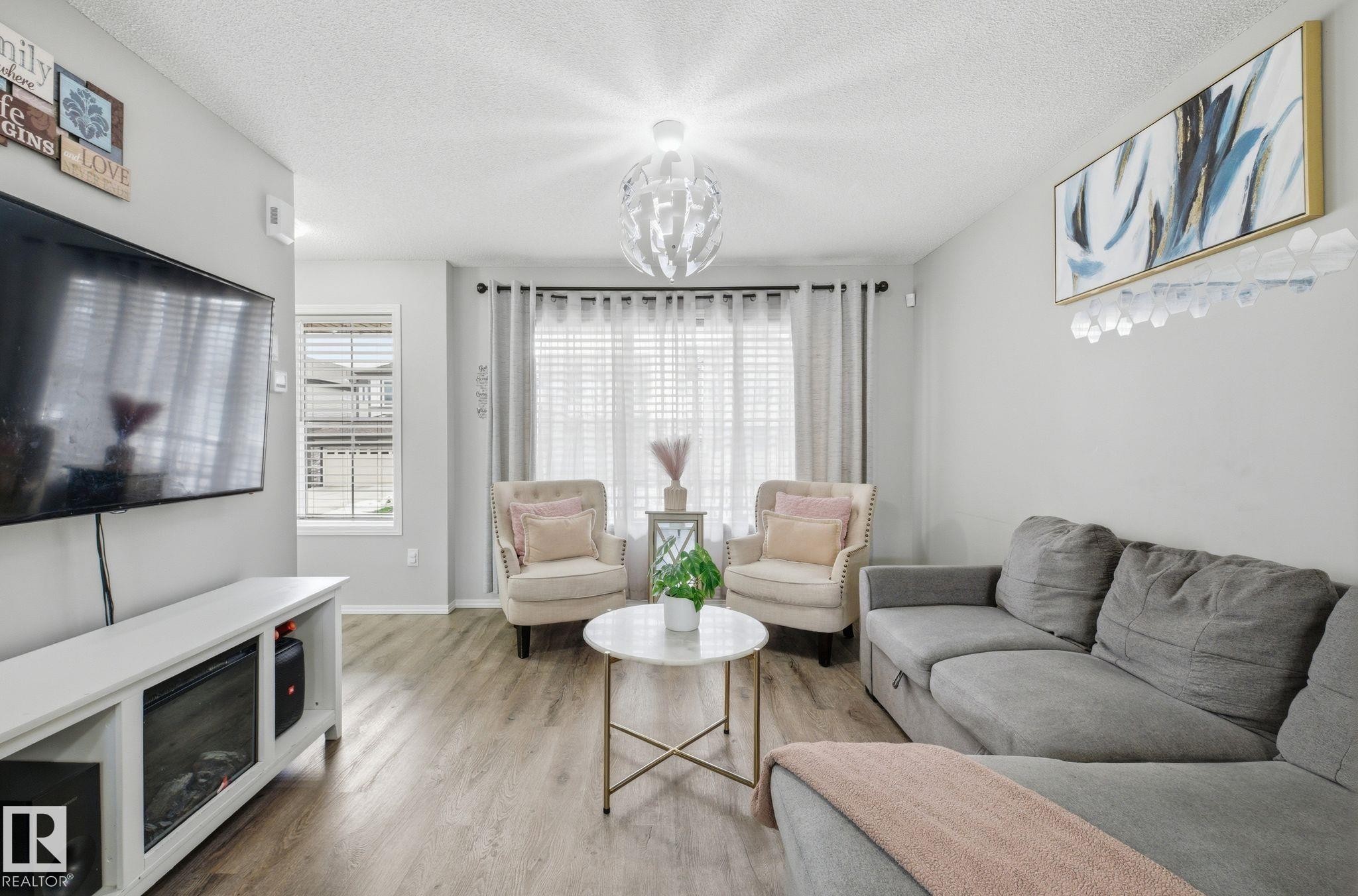 Living area featuring light gray walls, wood-style flooring, and a window with blinds and curtains - 4636 175 Ave, Edmonton, AB - Indoor Photo Showing Living Room With Fireplace