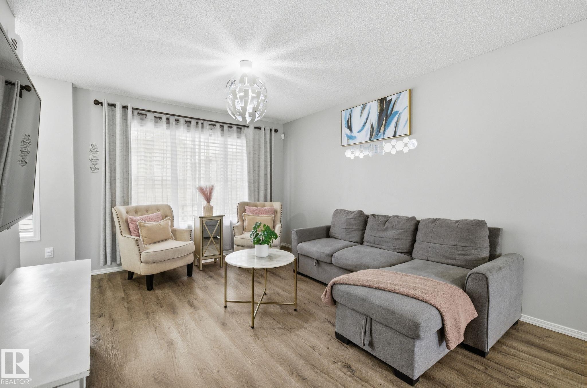 Living area featuring light wood-look flooring and a window with blinds and drapes - 4636 175 Ave, Edmonton, AB - Indoor Photo Showing Living Room