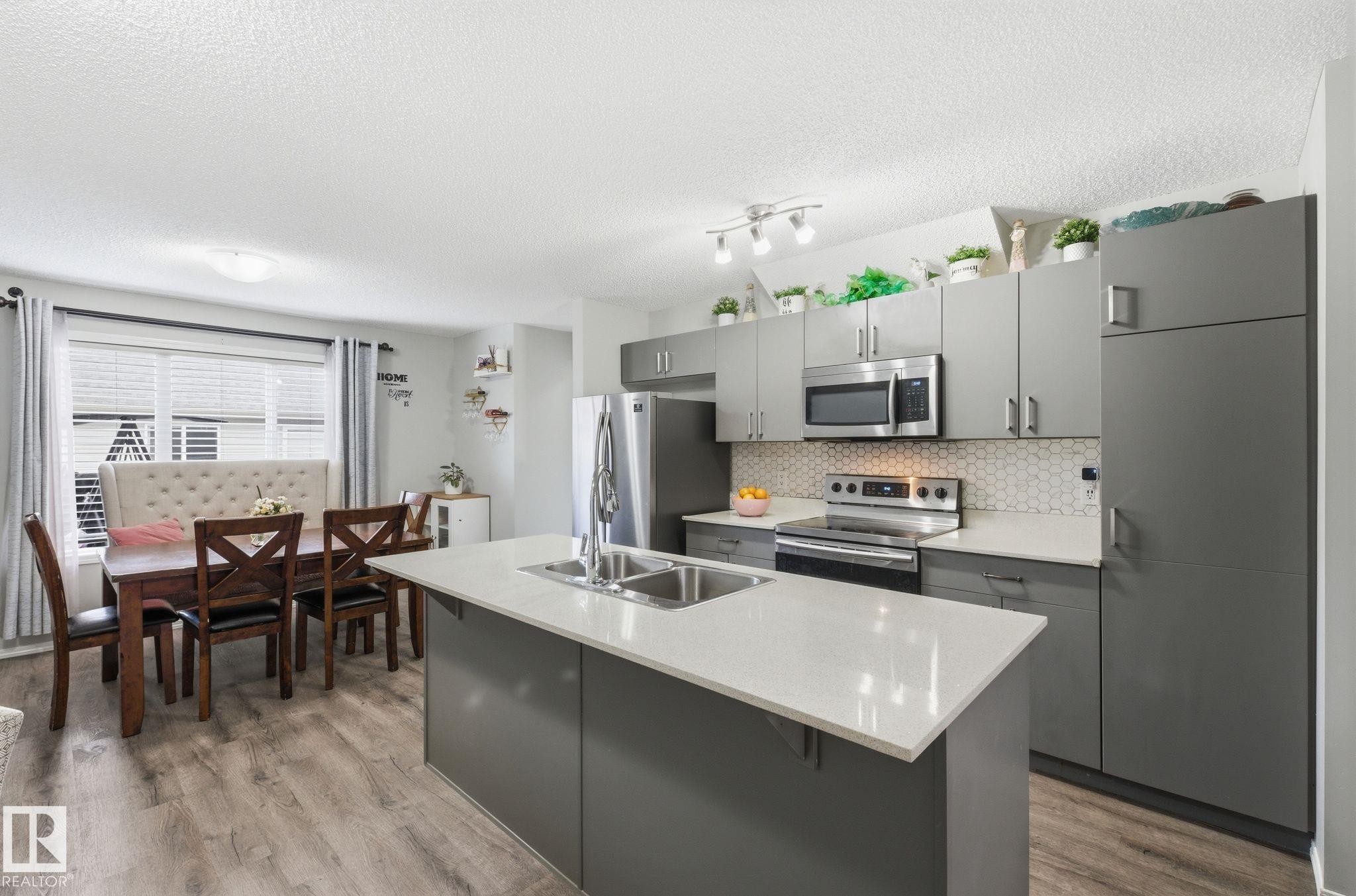 The kitchen features stainless steel appliances, grey cabinetry, and a white quartz countertop island with an integrated double sink - 4636 175 Ave, Edmonton, AB - Indoor Photo Showing Kitchen With Double Sink With Upgraded Kitchen