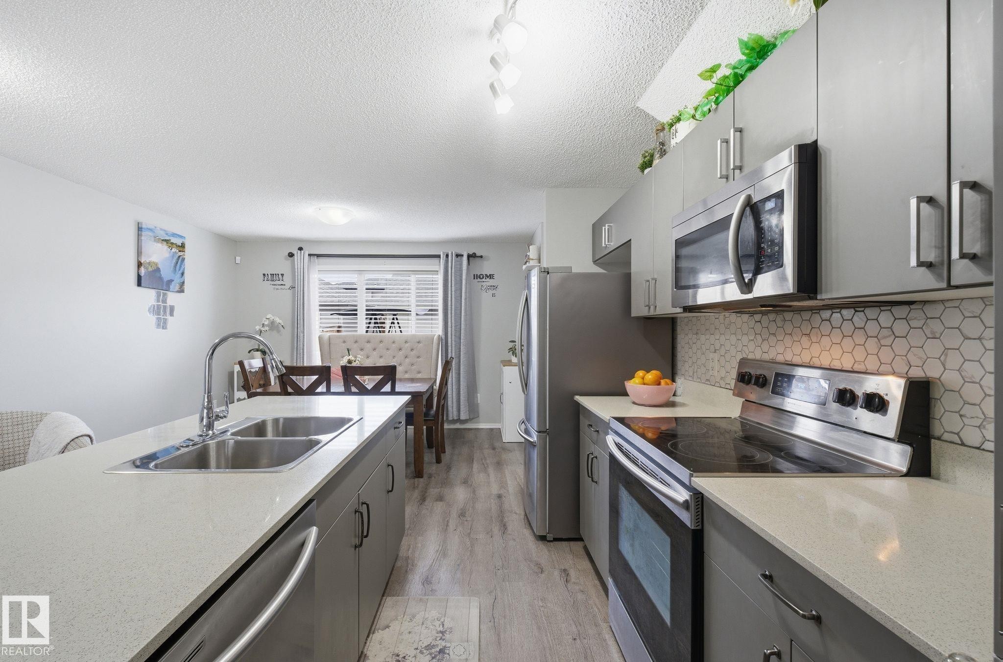 The kitchen features stainless steel appliances, grey cabinetry, light-colored countertops, and a white hexagonal tile backsplash - 4636 175 Ave, Edmonton, AB - Indoor Photo Showing Kitchen With Double Sink