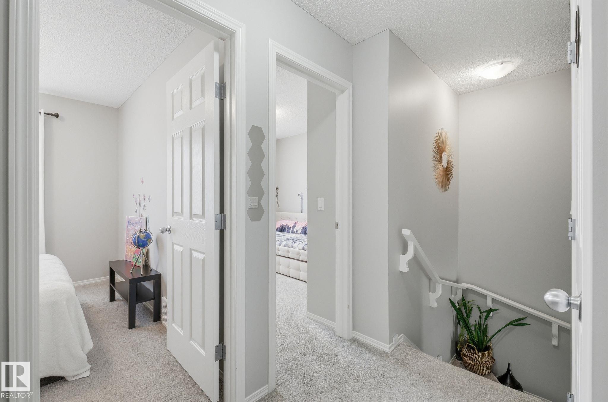The property features light gray walls and plush gray carpeting throughout the hallway, leading to a visible bed in one room and a partial view of another bed in a separate room - 4636 175 Ave, Edmonton, AB - Indoor Photo Showing Other Room