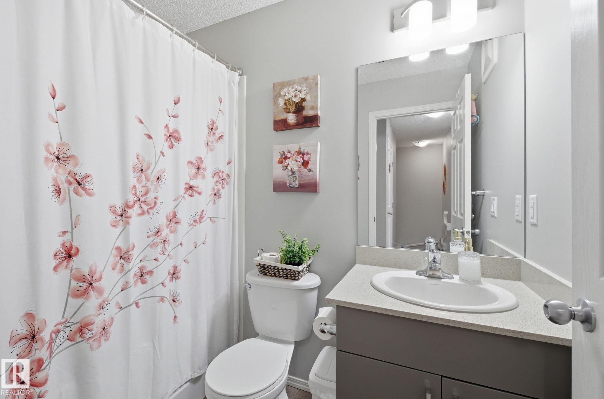 The bathroom features a toilet, a vanity with a sink and a mirror, and a shower with a shower curtain - 4636 175 Ave, Edmonton, AB - Indoor Photo Showing Bathroom