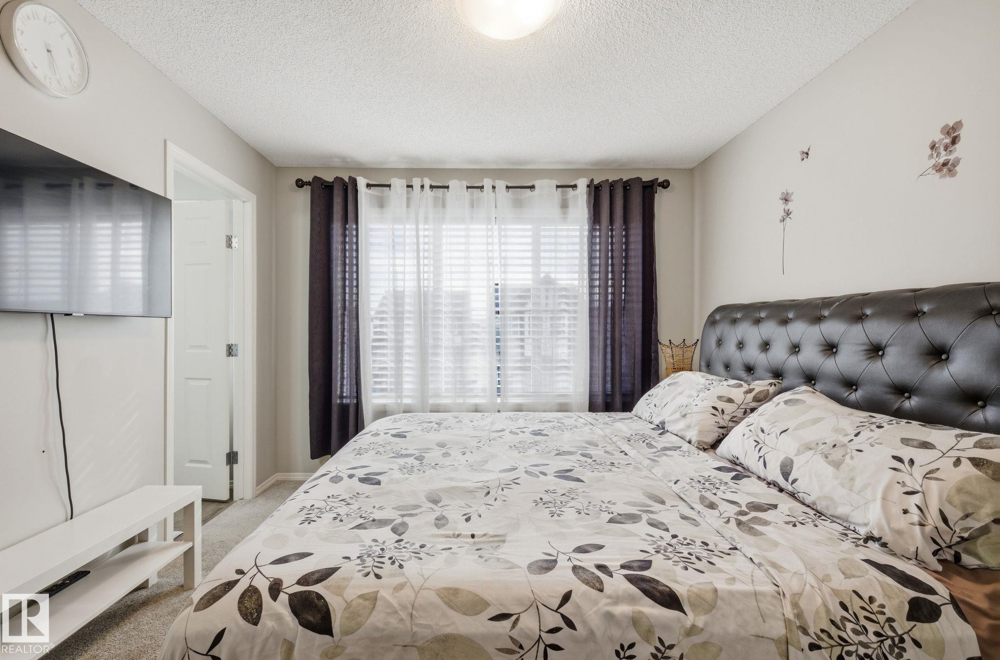 This bedroom features a window with blinds and dark curtains, light-colored walls, and a textured ceiling - 4636 175 Ave, Edmonton, AB - Indoor Photo Showing Bedroom
