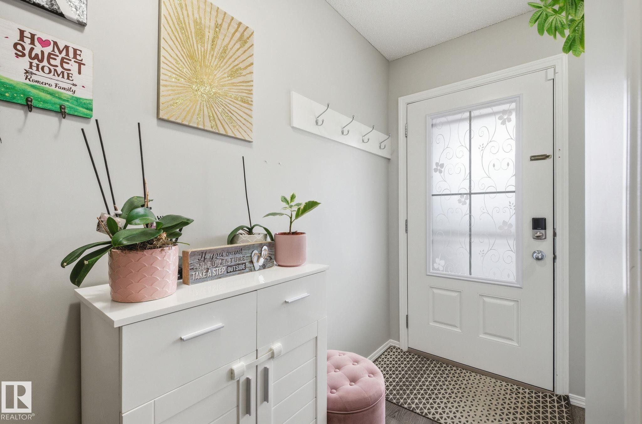 The property features a white entry door with decorative privacy glass, a white shoe cabinet with horizontal handles, and a white coat rack with five hooks - 4636 175 Ave, Edmonton, AB - Indoor Photo Showing Other Room