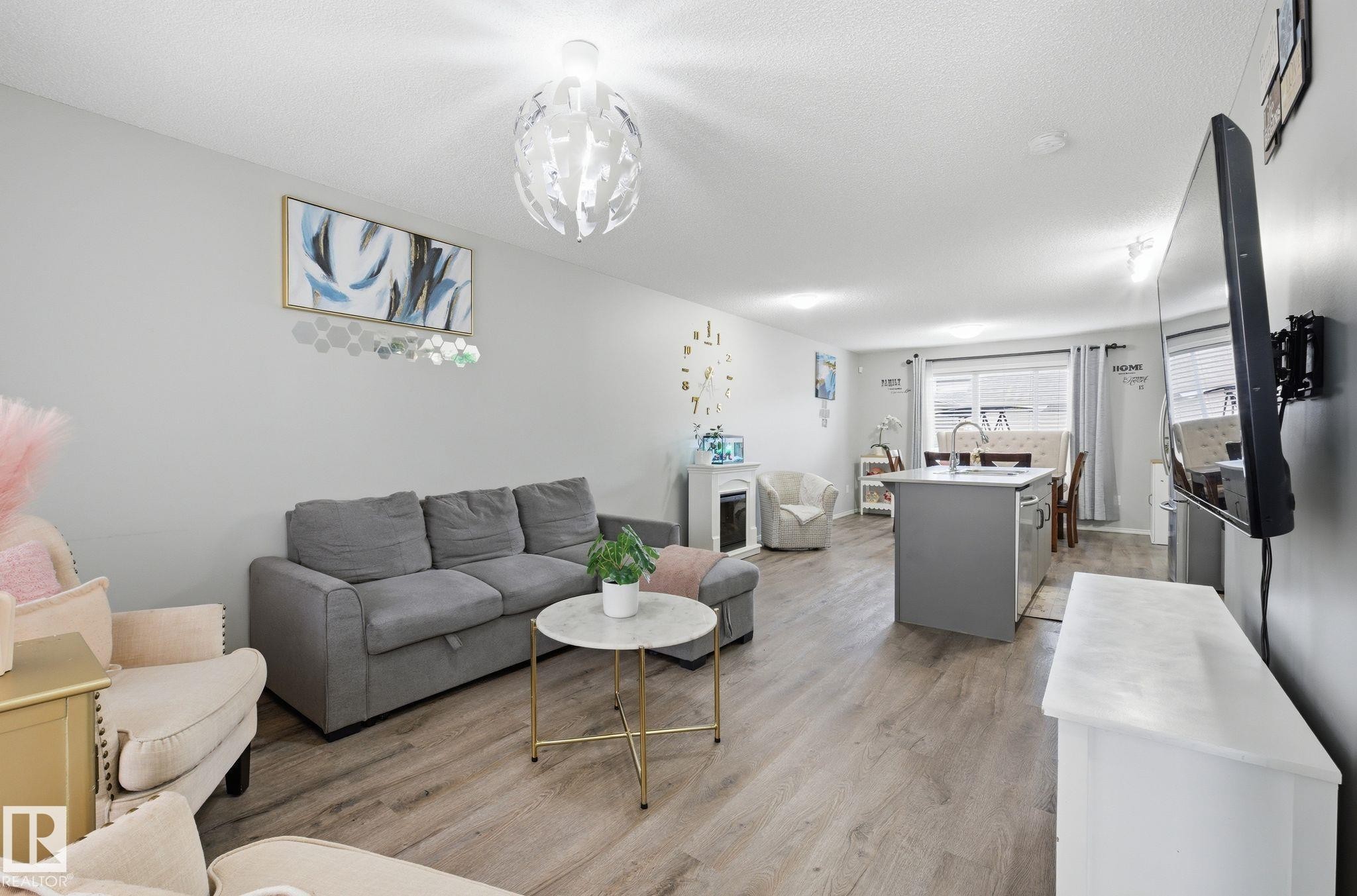 Open concept living area featuring light-toned flooring, a modern light fixture, and a kitchen island with a sink - 4636 175 Ave, Edmonton, AB - Indoor Photo Showing Living Room