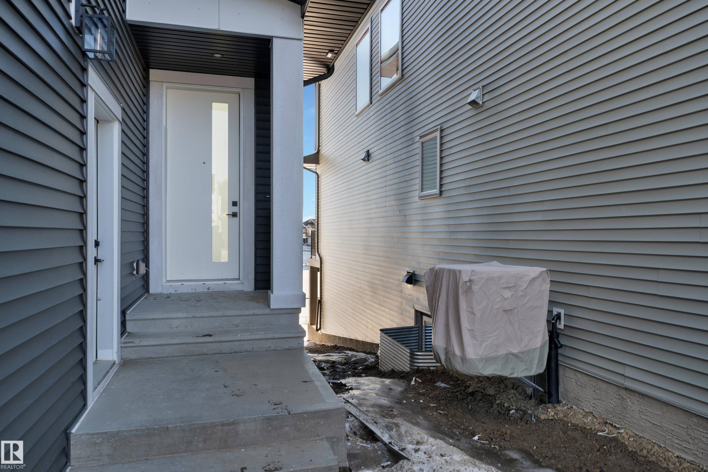 Modern entry featuring a white door with vertical glass insert, concrete steps, and dark siding with white trim - 226 Linden Loop, Leduc, AB - Outdoor With Exterior