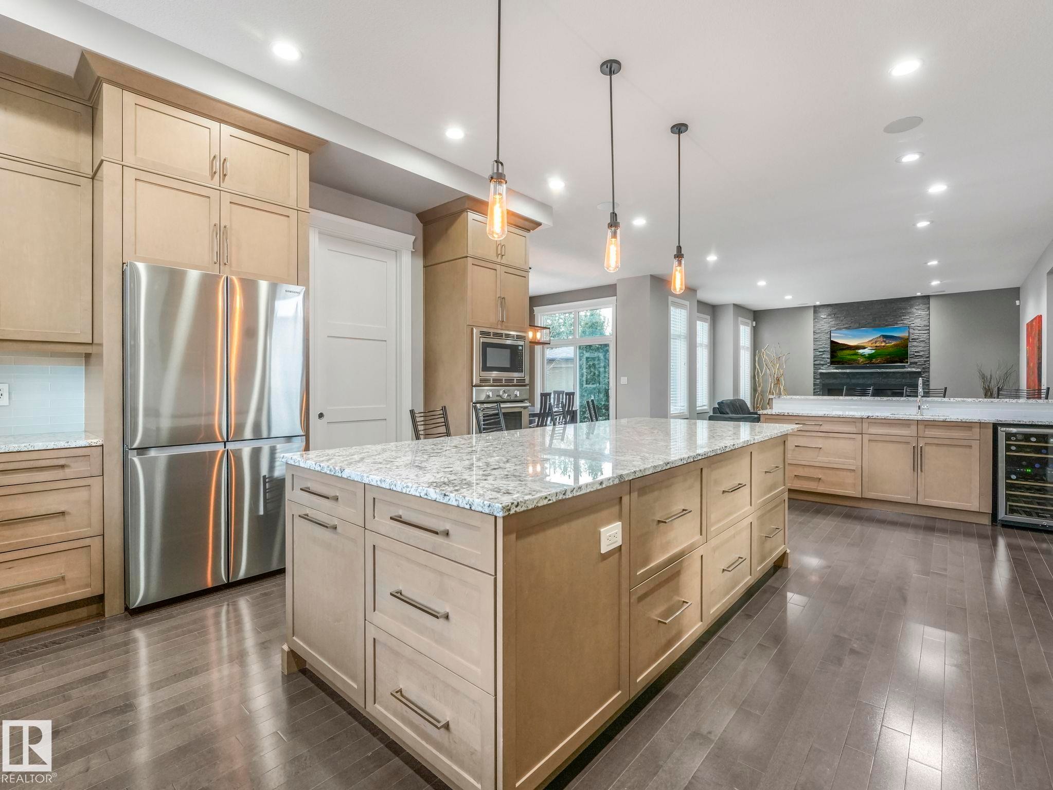 Open-concept kitchen featuring an expansive center island with granite countertop, integrated stainless steel appliances, extensive cabinetry, and wood-finish flooring - 8927 120 Street Nw, Edmonton, AB - Indoor Photo Showing Kitchen With Upgraded Kitchen