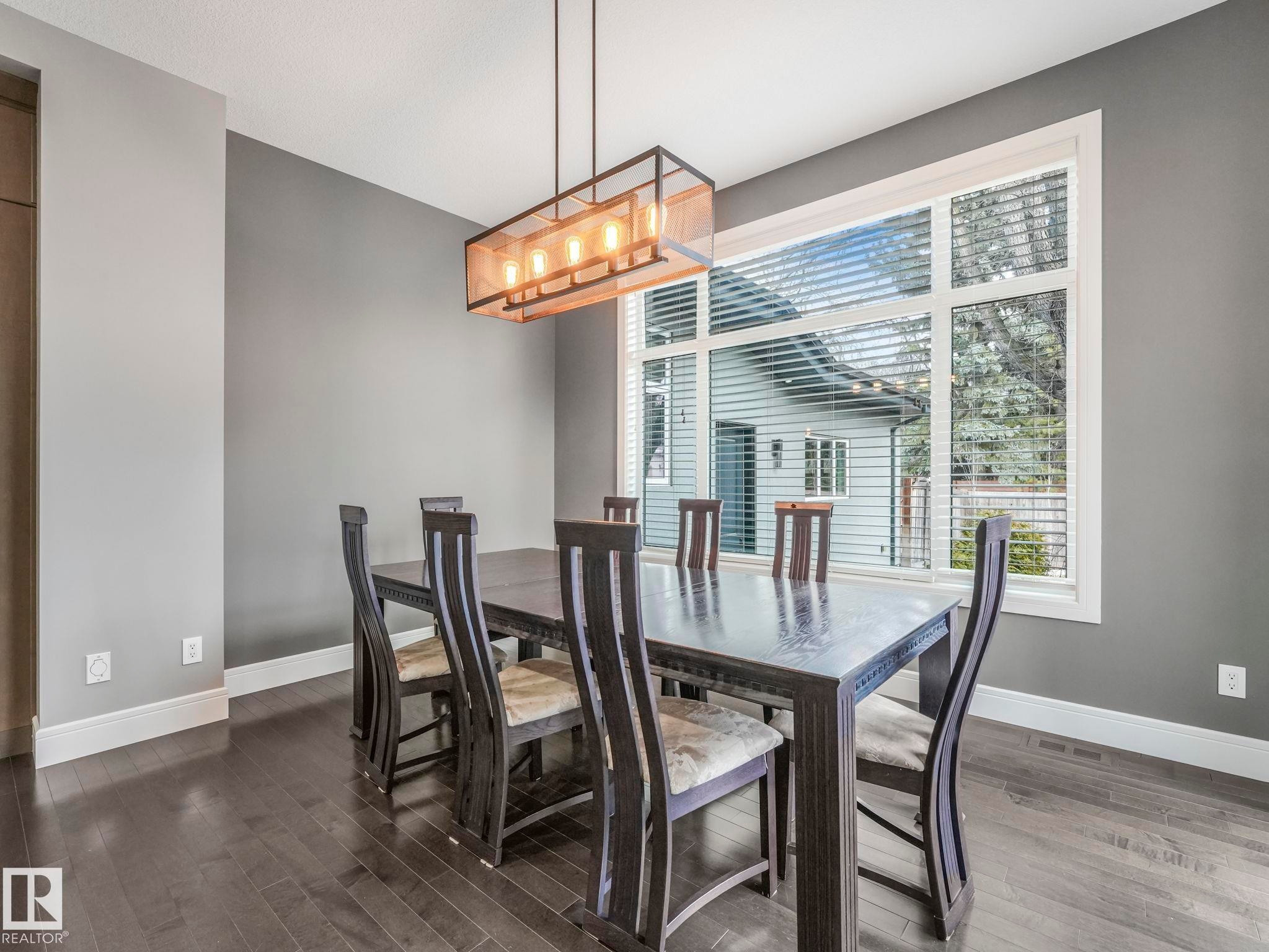 Dining area featuring a large window, dark wood-finish flooring, a contemporary linear chandelier, and a neutral wall color with white trim - 8927 120 Street Nw, Edmonton, AB - Indoor Photo Showing Dining Room