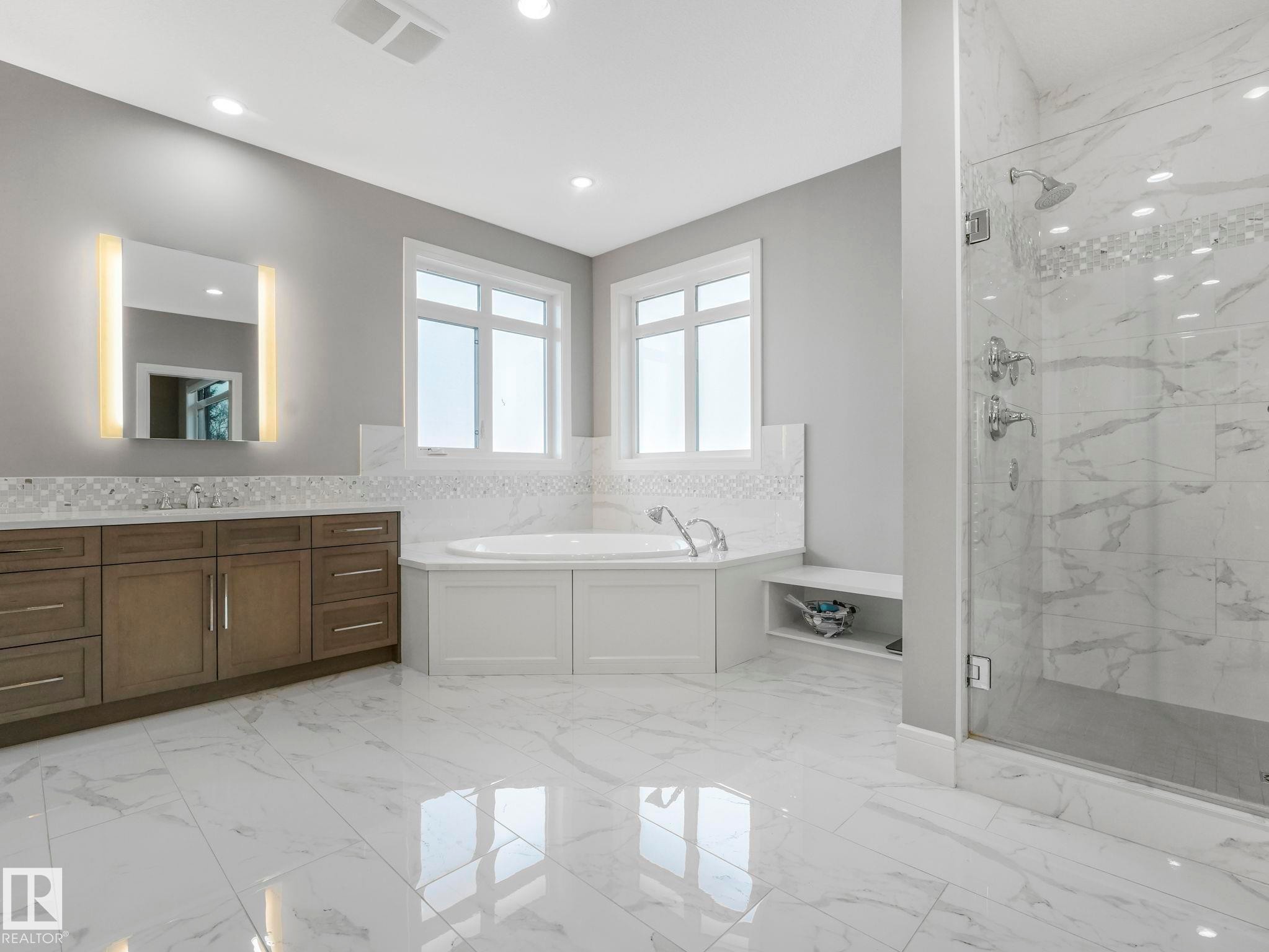 Spacious bathroom featuring large format marble-look tile flooring, dual-pane windows, a built-in corner soaking tub, a frameless glass shower enclosure, and a vanity with integrated lighting - 8927 120 Street Nw, Edmonton, AB - Indoor Photo Showing Bathroom