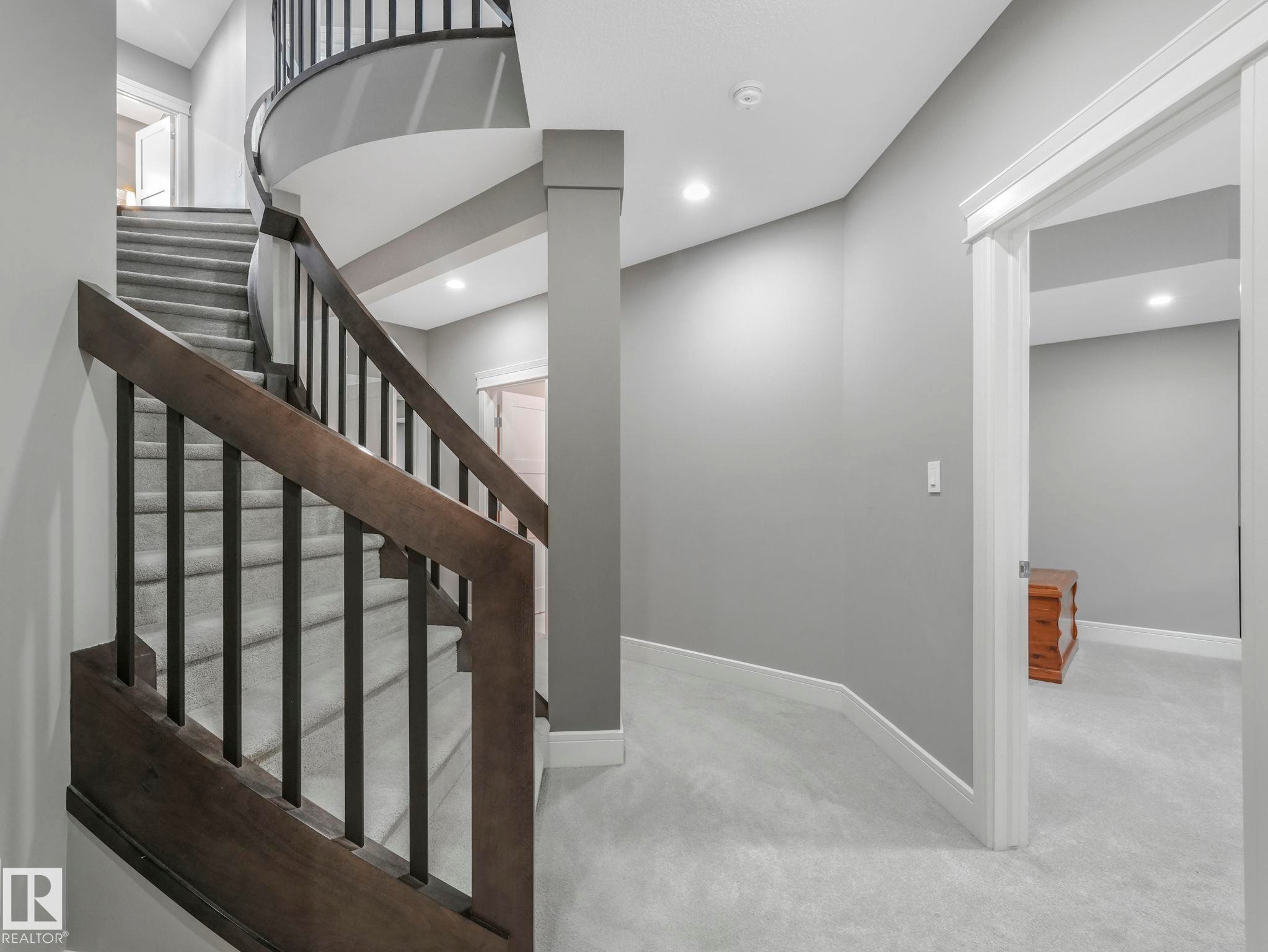 Curved staircase featuring dark wood newel posts and handrails with black metal balusters - 8927 120 Street Nw, Edmonton, AB - Indoor Photo Showing Other Room