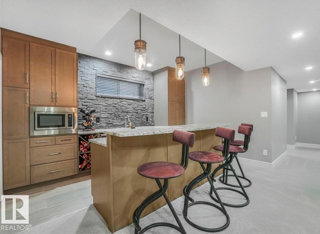Integrated bar area featuring a granite countertop, stone accent wall, recessed lighting, and wood-finish cabinetry with a built-in microwave and wine rack - 8927 120 Street Nw, Edmonton, AB - Indoor Photo Showing Kitchen