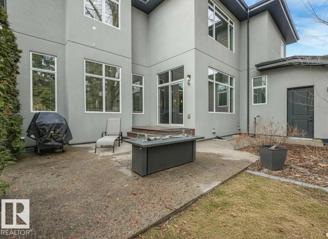Rear exterior featuring a large concrete patio, an elevated wood deck, and multiple oversized windows with white frames - 8927 120 Street Nw, Edmonton, AB - Outdoor With Exterior