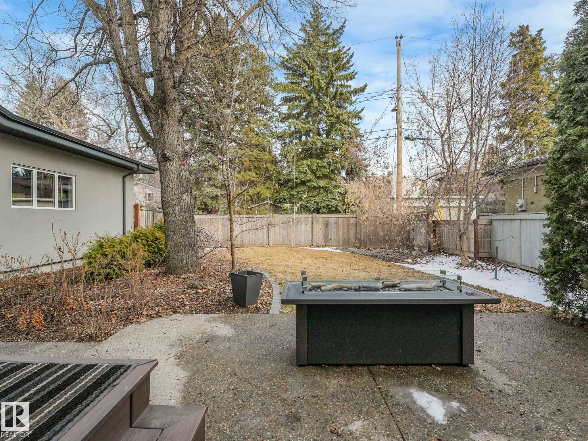 Expansive concrete patio with a built-in fire pit, surrounded by a fenced yard and mature landscaping - 8927 120 Street Nw, Edmonton, AB - Outdoor