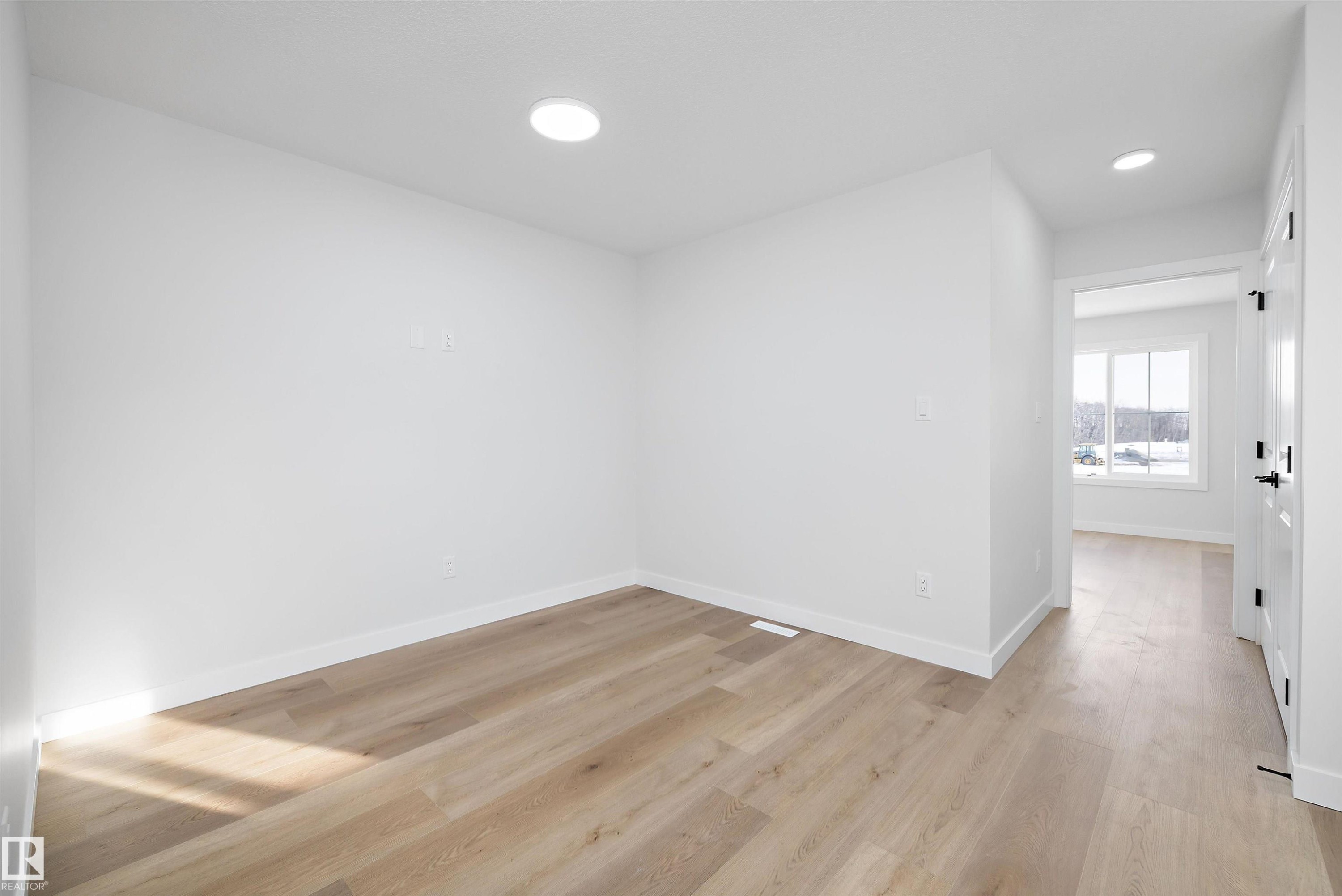 Bright interior room featuring wood-finish flooring, recessed lighting, white baseboards, and a white interior door with black hardware - 954 Elderberry Landing, Edmonton, AB - Indoor Photo Showing Other Room