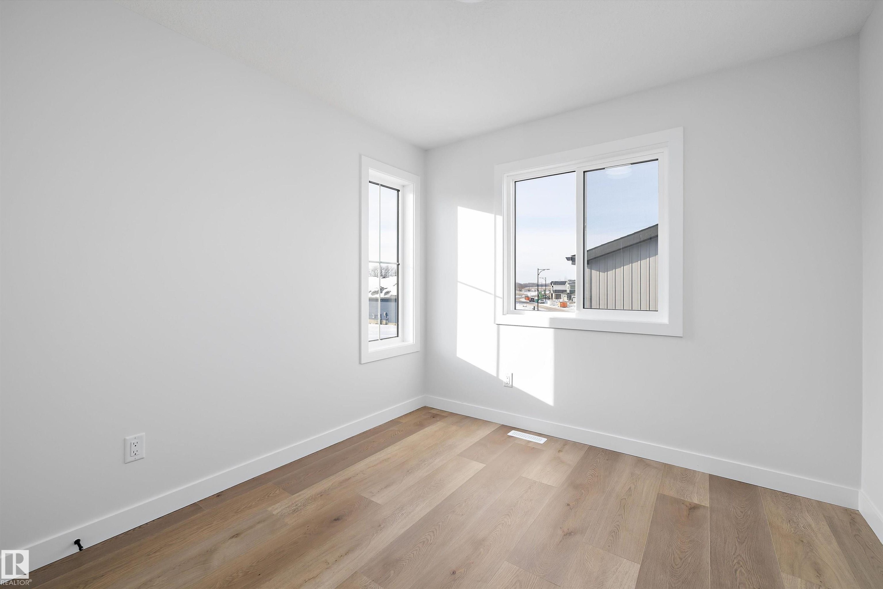Bright room with wood-finish flooring, white baseboards, and two windows with white trim - 954 Elderberry Landing, Edmonton, AB - Indoor Photo Showing Other Room