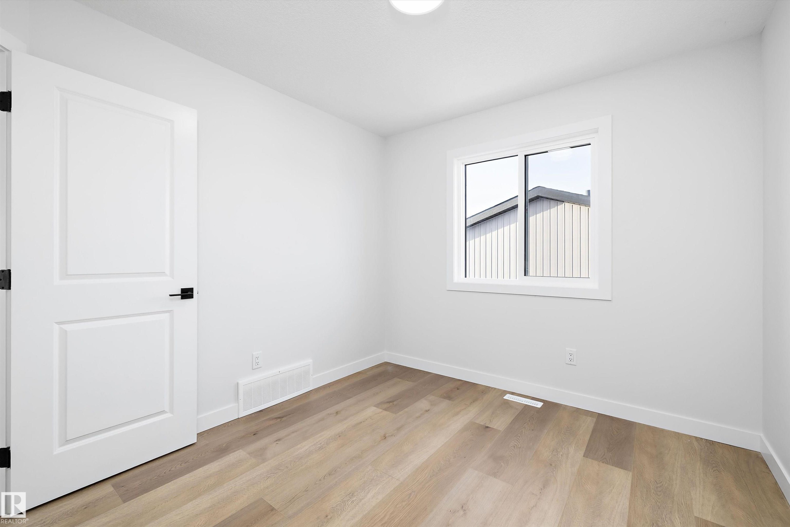 Light-filled room featuring durable wood-finish flooring, a white interior door with matte black hardware, and a single window offering natural light - 954 Elderberry Landing, Edmonton, AB - Indoor Photo Showing Other Room