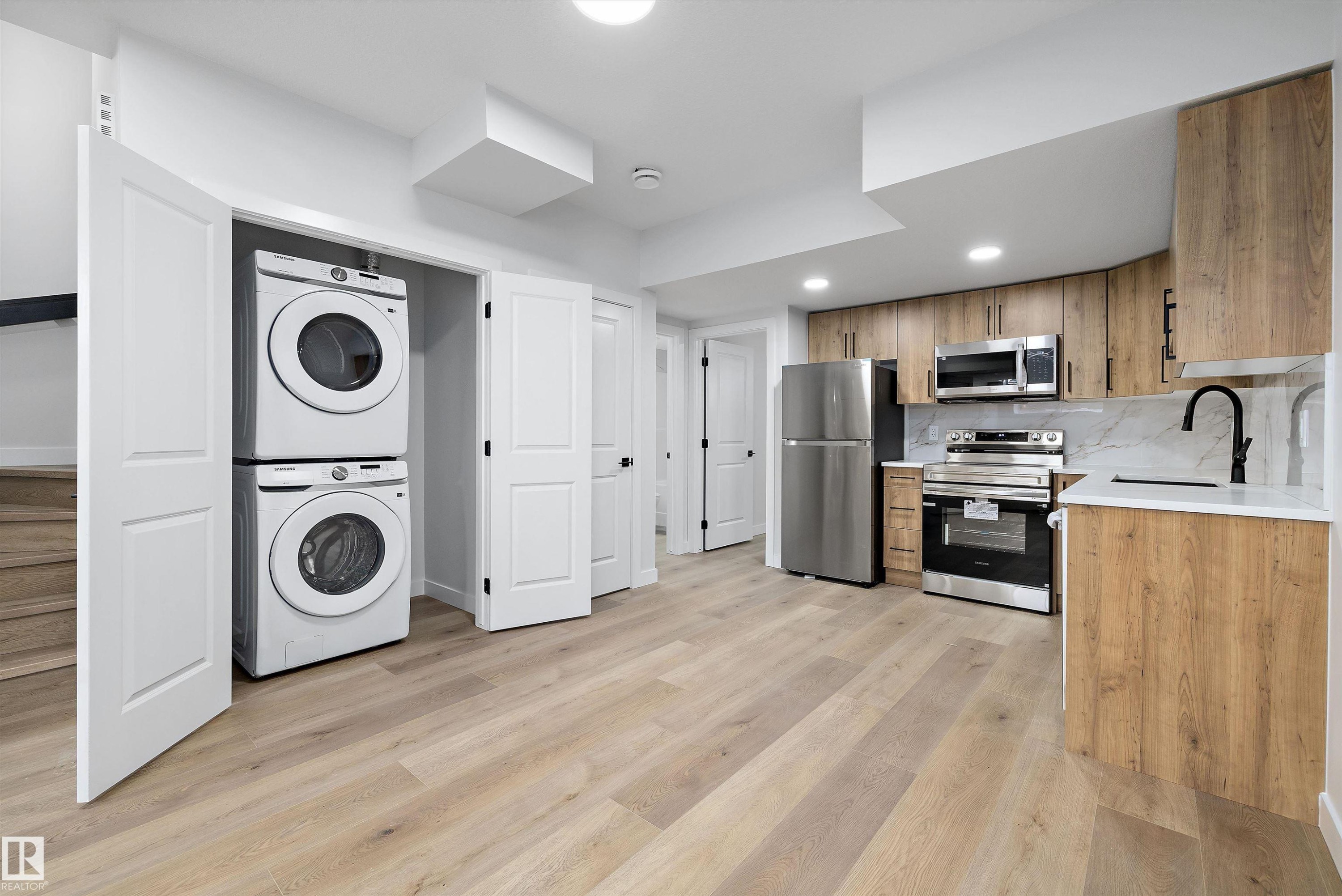 Modern kitchen featuring wood-finish cabinetry, stainless steel appliances, and a marble-finish backsplash - 954 Elderberry Landing, Edmonton, AB - Indoor Photo Showing Laundry Room