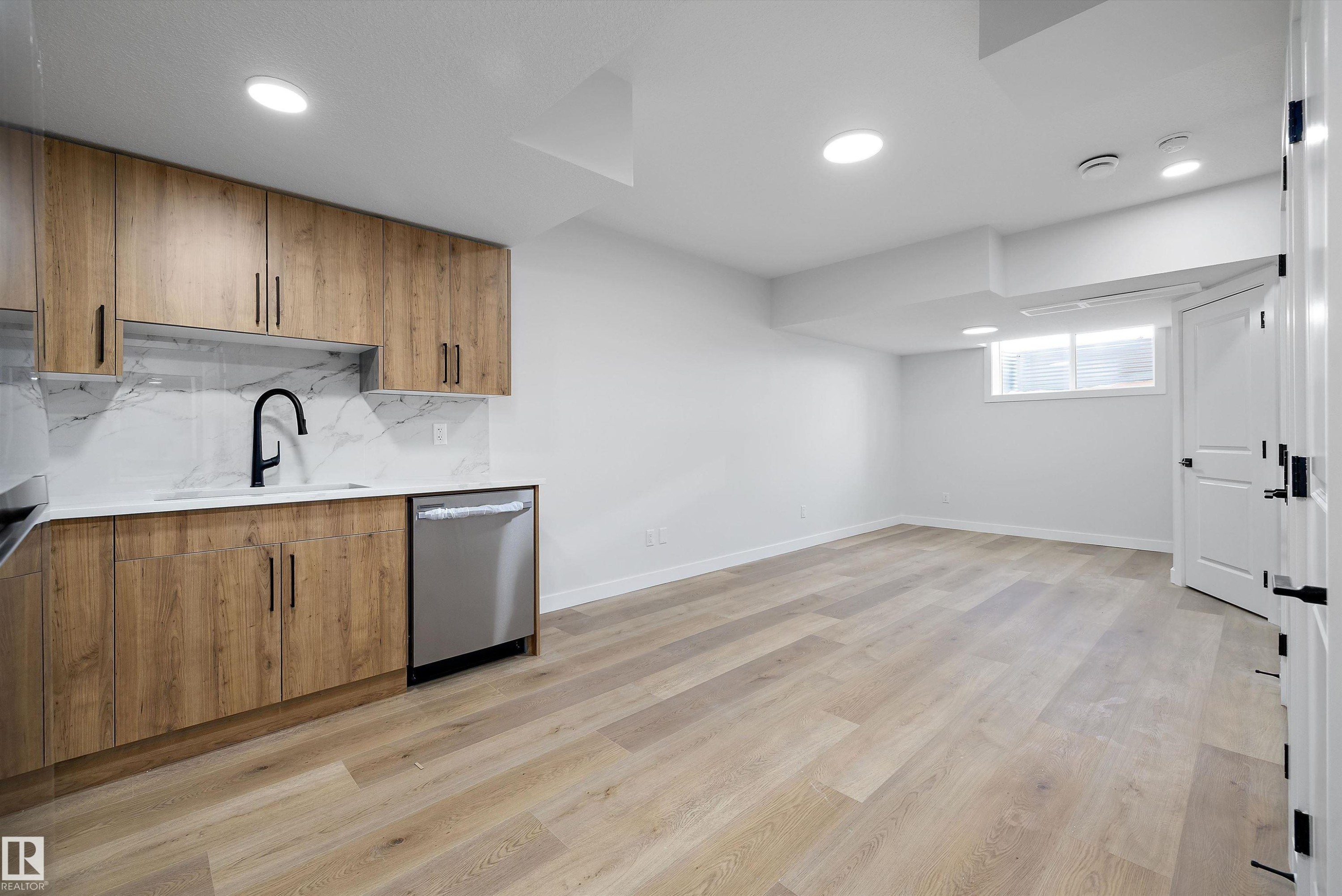 Kitchenette featuring wood-finish cabinetry, a stainless steel dishwasher, a matte black faucet, and a white marble-patterned backsplash - 954 Elderberry Landing, Edmonton, AB - Indoor Photo Showing Kitchen